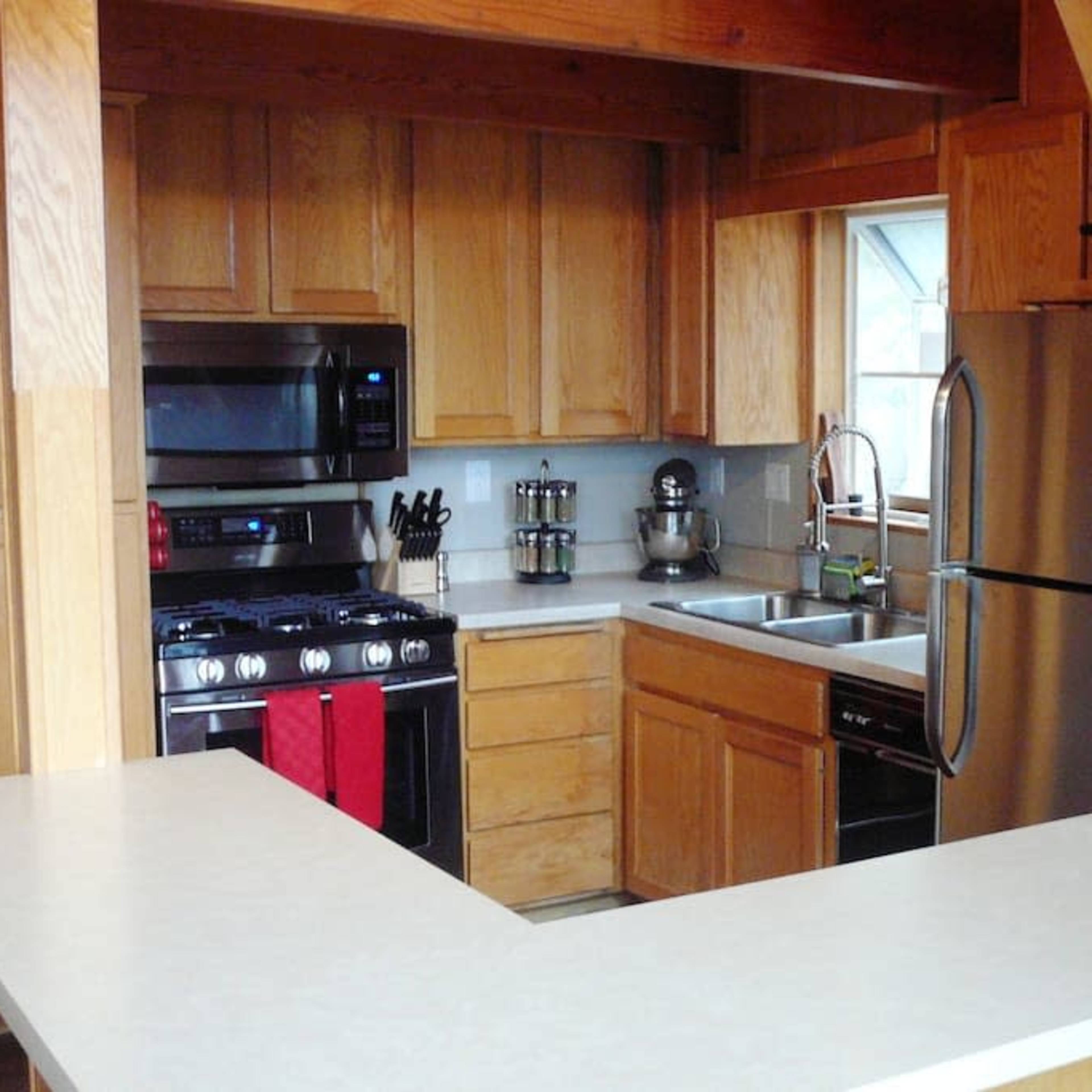 A wooden kitchen with modern appliances, including a gas stove, refrigerator, and a sink, along with a countertop and cabinets.