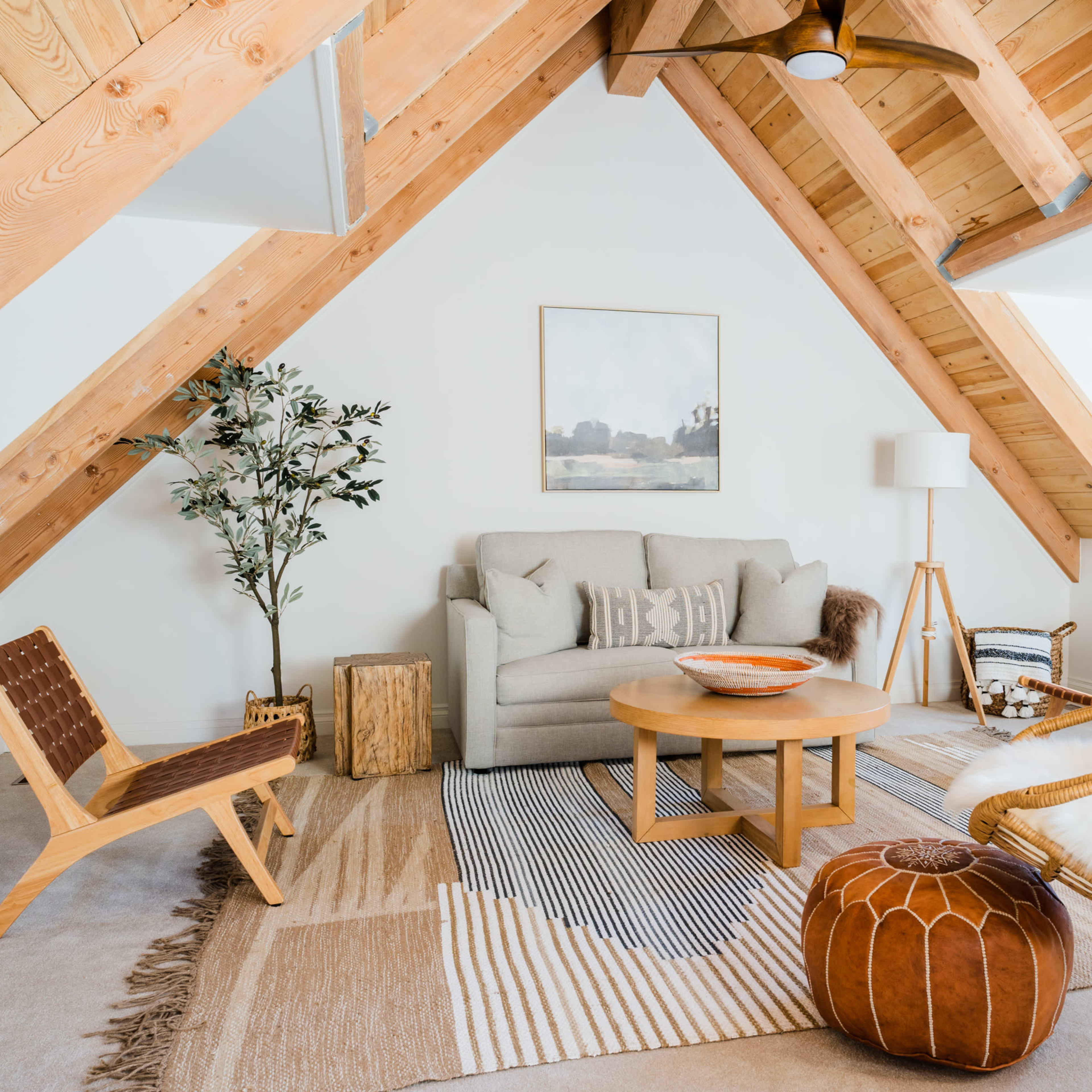 A cozy attic living space featuring a hanging chair, a wooden table, a sofa, and modern decor under a sloped wooden ceiling.