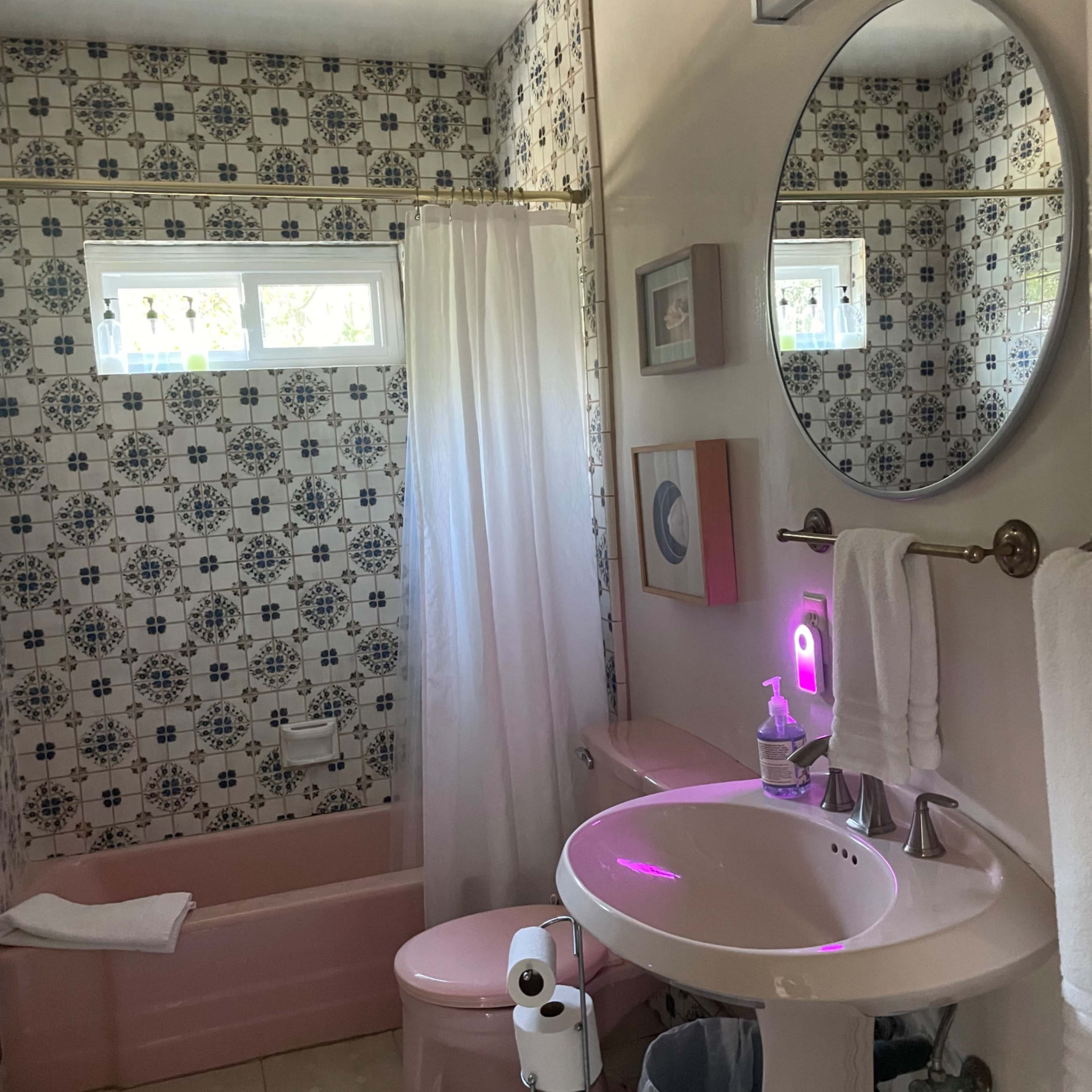 A bathroom with a pink bathtub and toilet, a white sink with a circular mirror, and patterned tile walls.