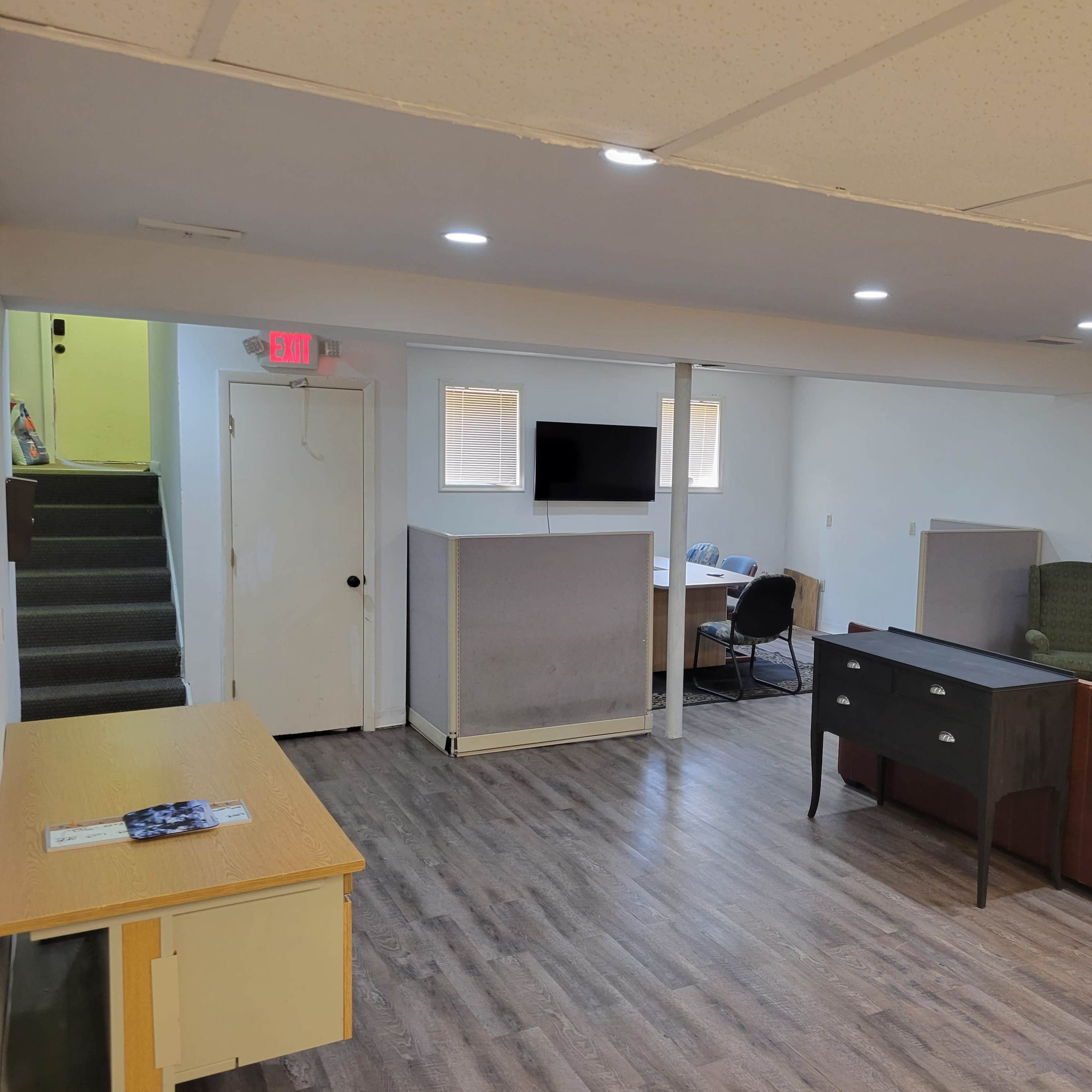A spacious basement area with a desk, chair, sofa, and bookshelves, along with a staircase leading to another level.