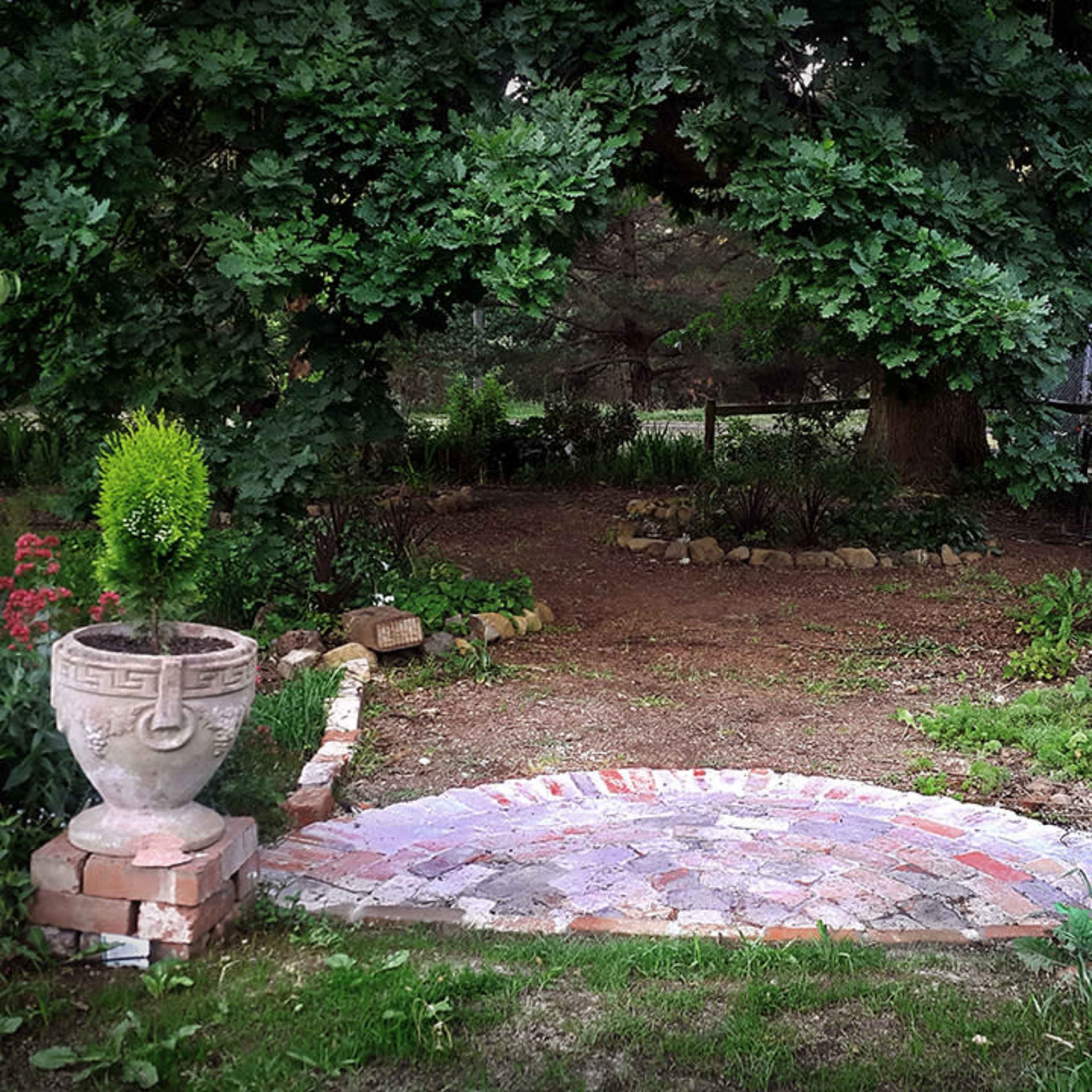 A stone path leads to a garden adorned with decorative urns and surrounded by greenery and flowering plants.