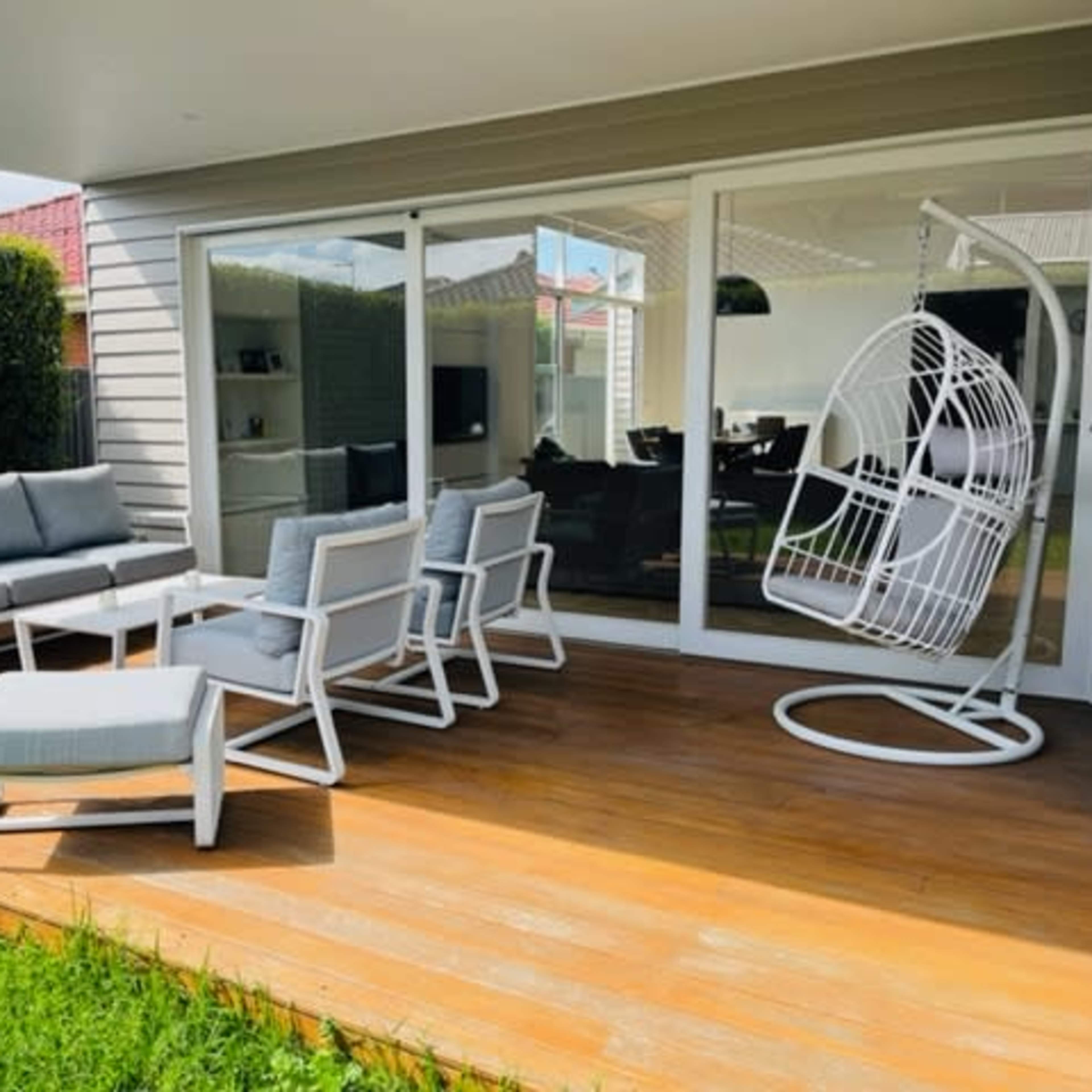 A modern outdoor seating area with a sofa, chairs, and a hanging swing, situated on a wooden deck next to large glass doors.