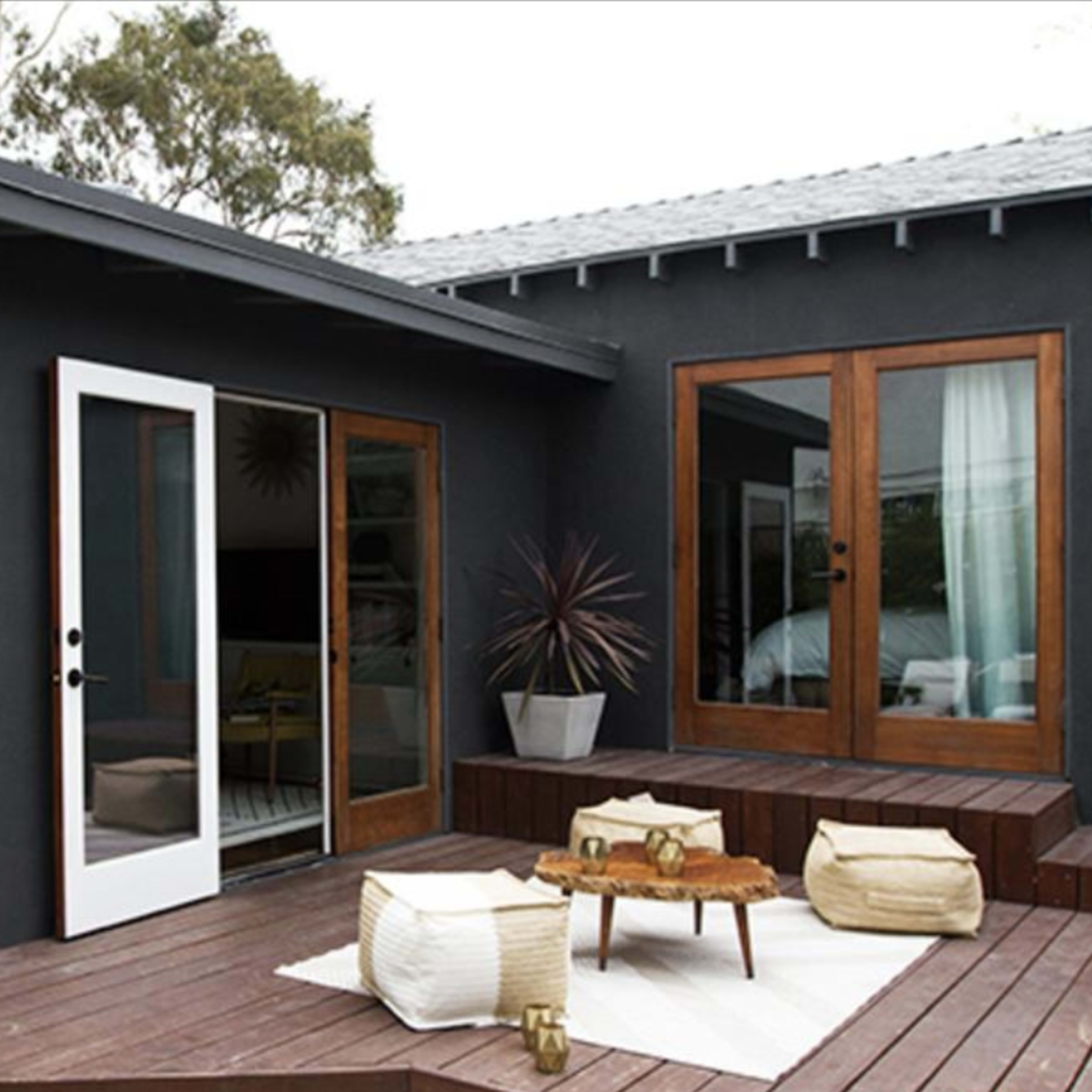 A modern outdoor patio area with wooden steps leading up to a home featuring large glass doors and a small table surrounded by seating.