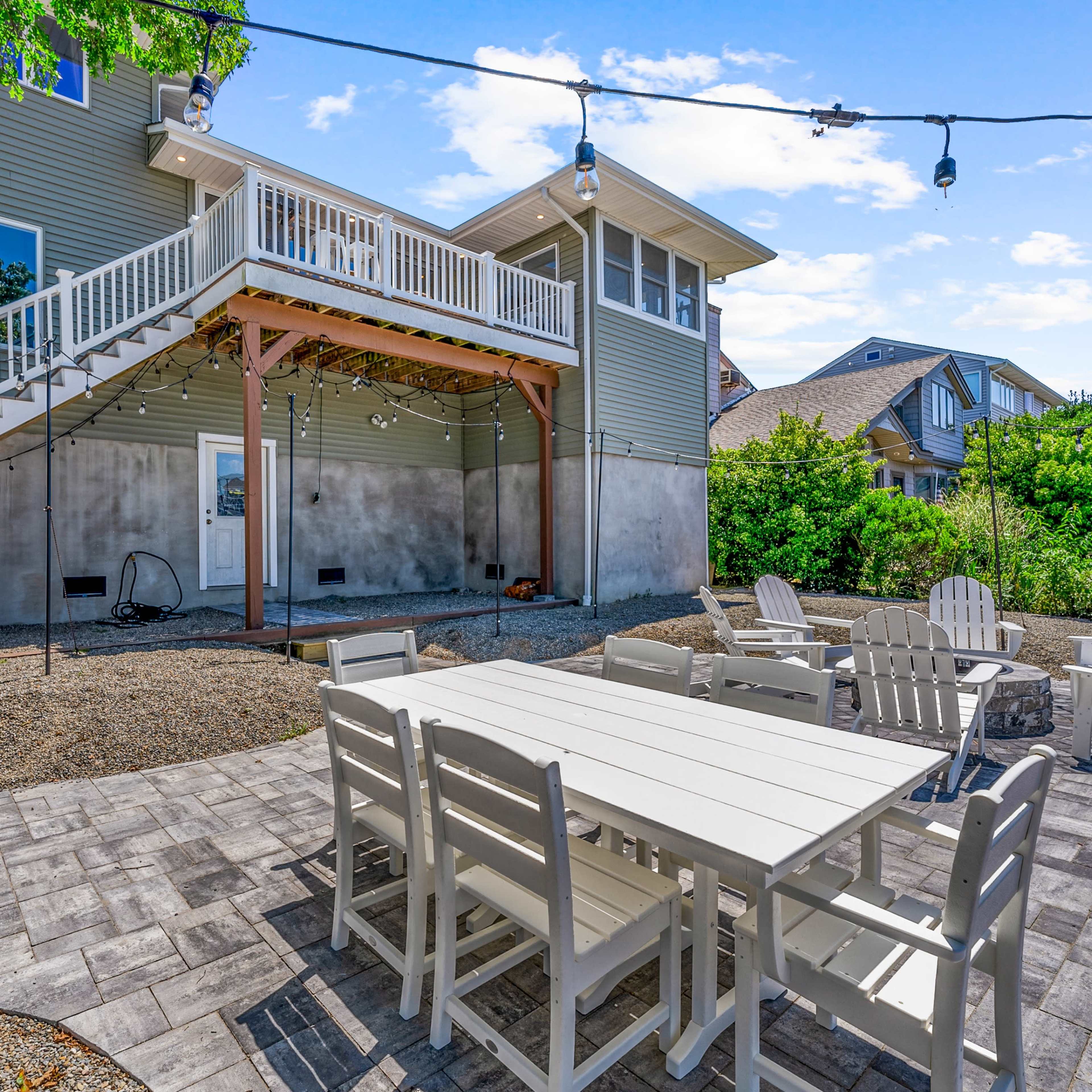 A backyard patio area with a white dining table surrounded by chairs, gravel ground, and a house with a large elevated deck.