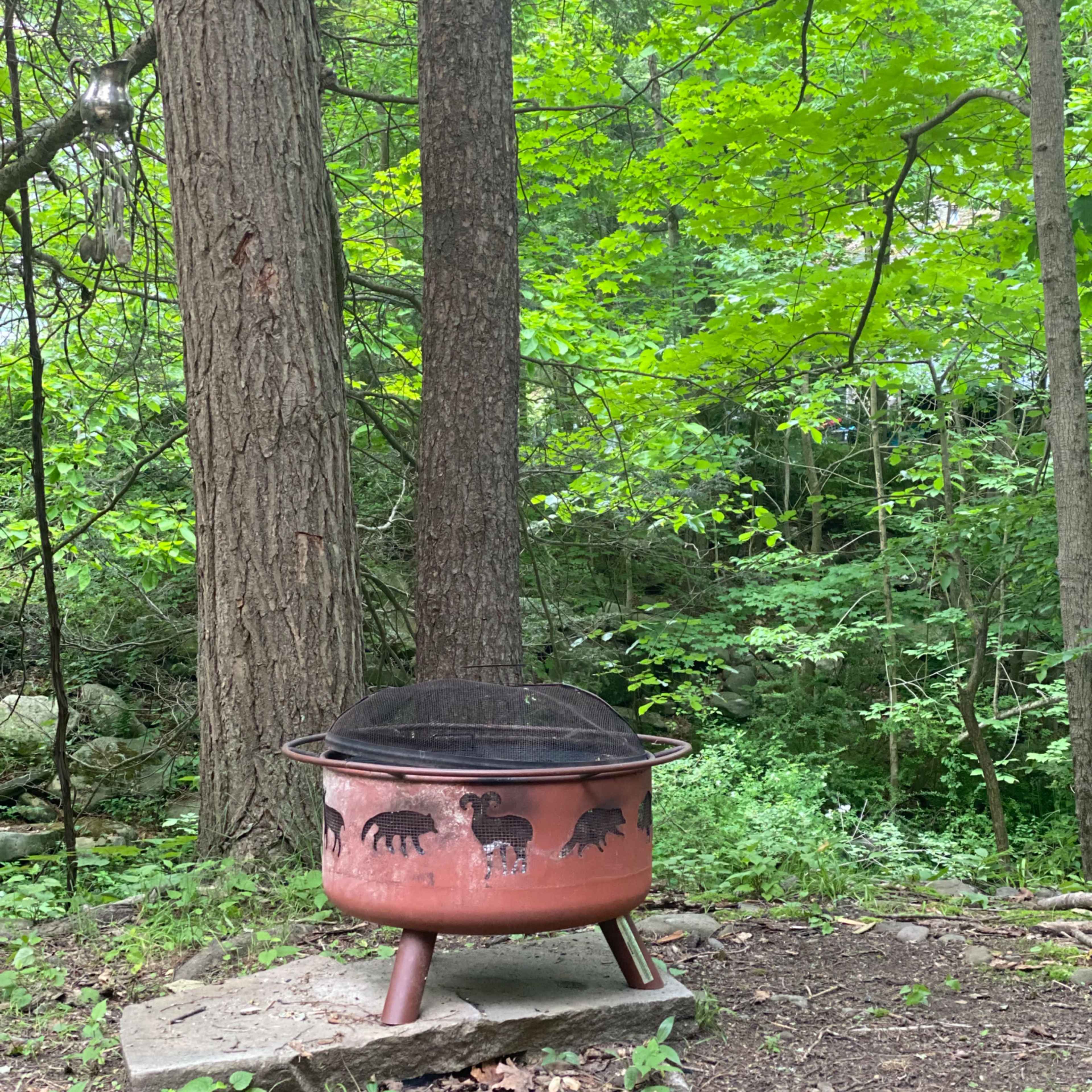 A ceramic fire pit with animal designs sits on a stone base surrounded by trees and greenery.