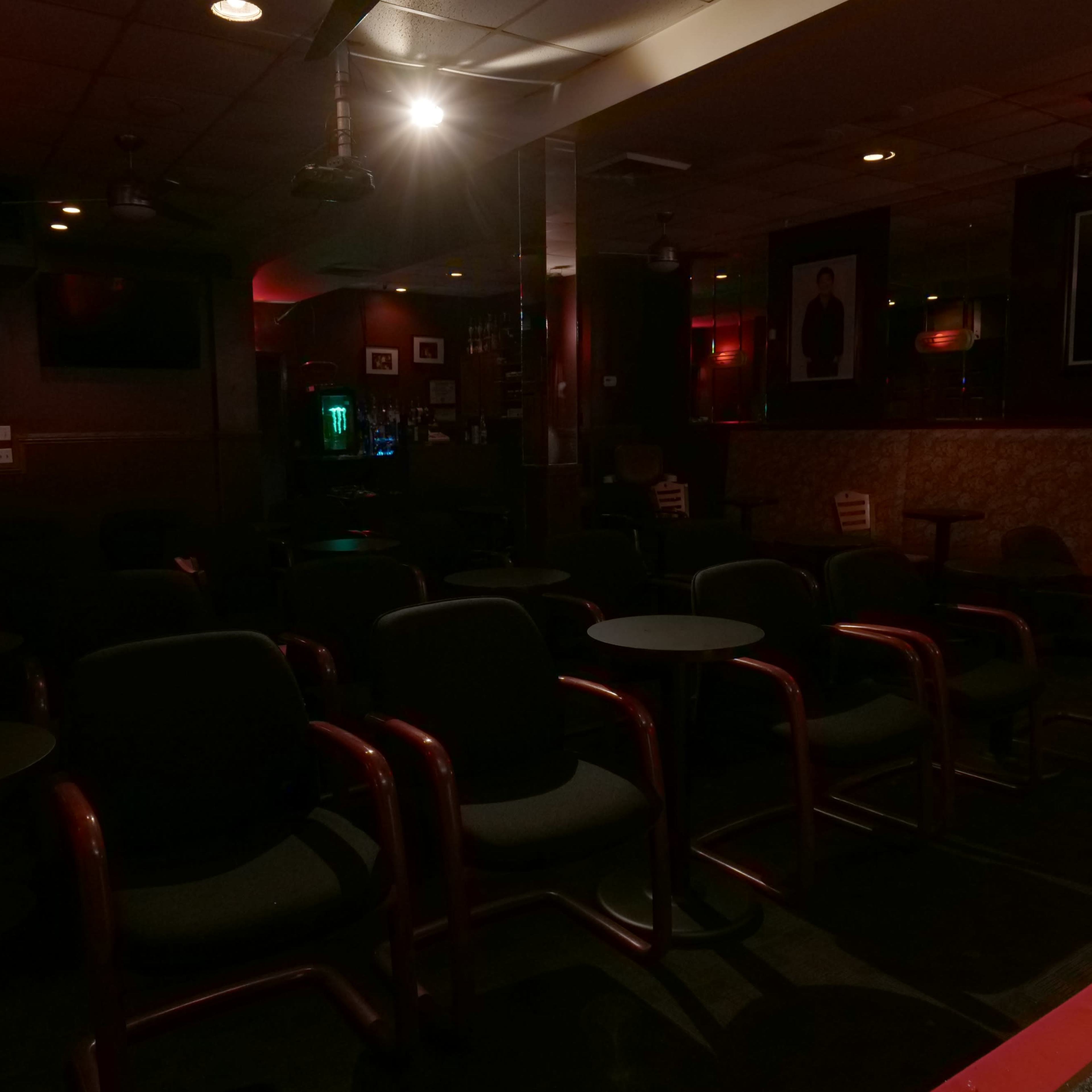 A dimly lit lounge features empty chairs and tables arranged in rows against red-tinted walls.