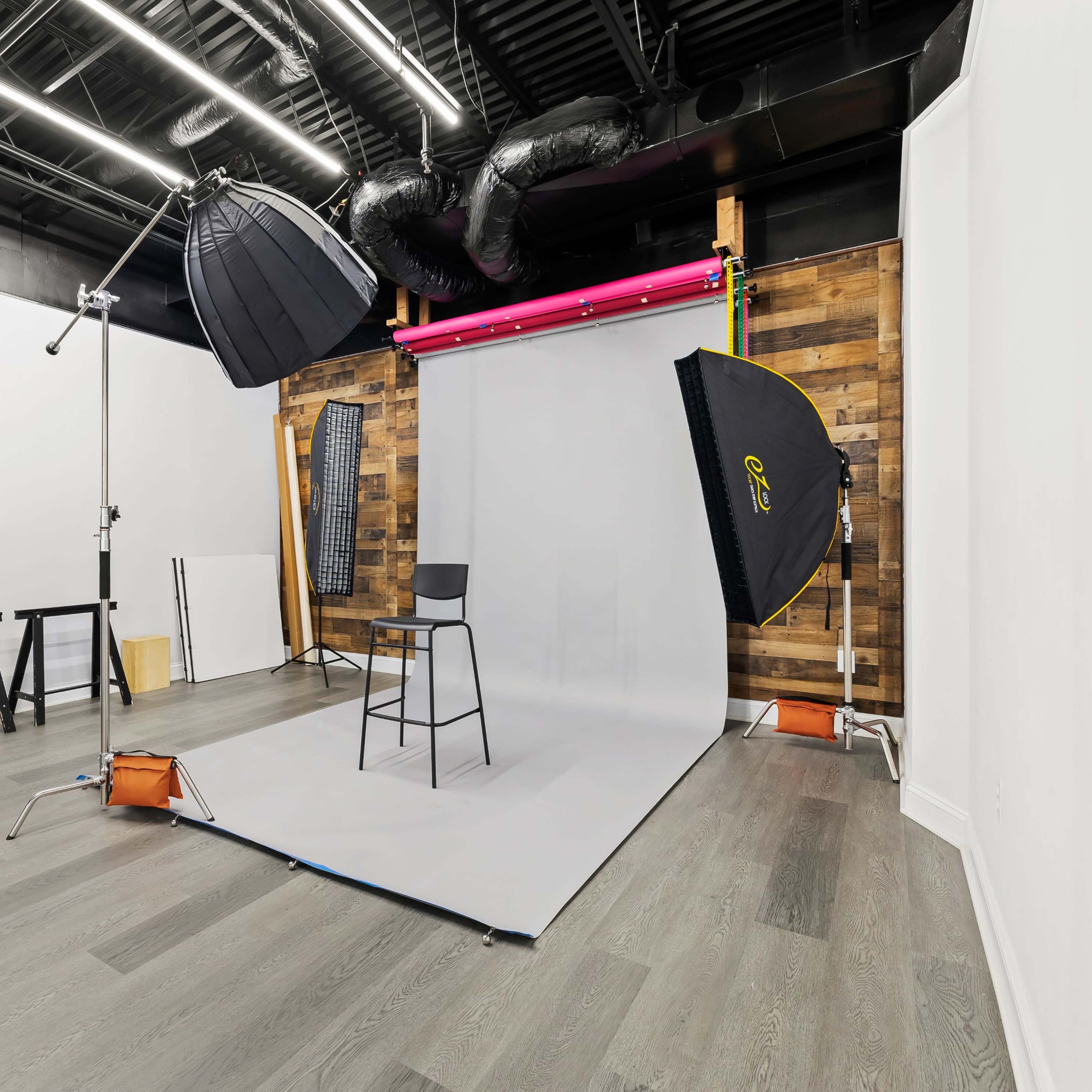 A photography studio with a gray backdrop, a black chair, and various lighting equipment set up in a modern interior space.