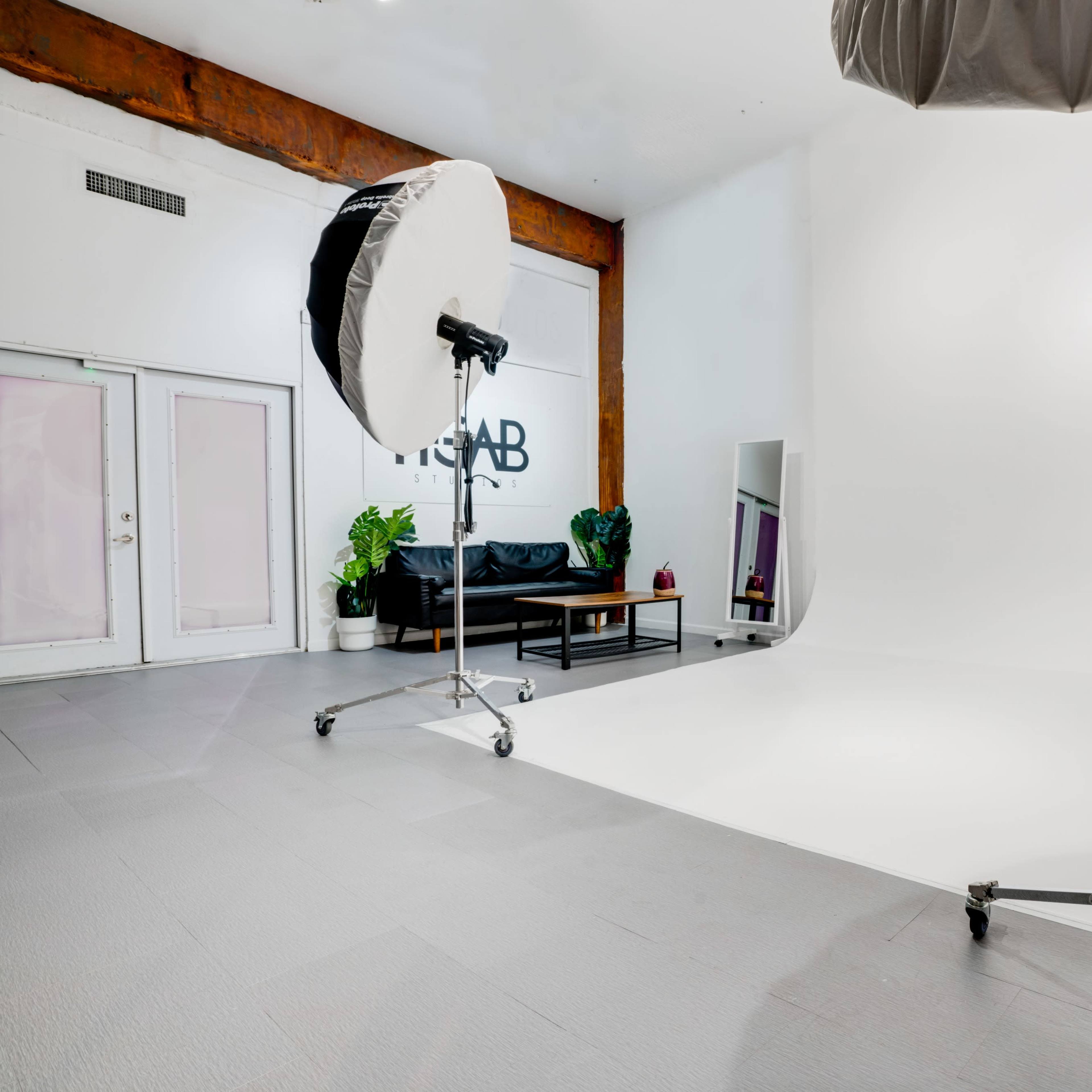 A photography studio with large softboxes, a white backdrop, and a black couch against a wall with the word "STAB" visible.