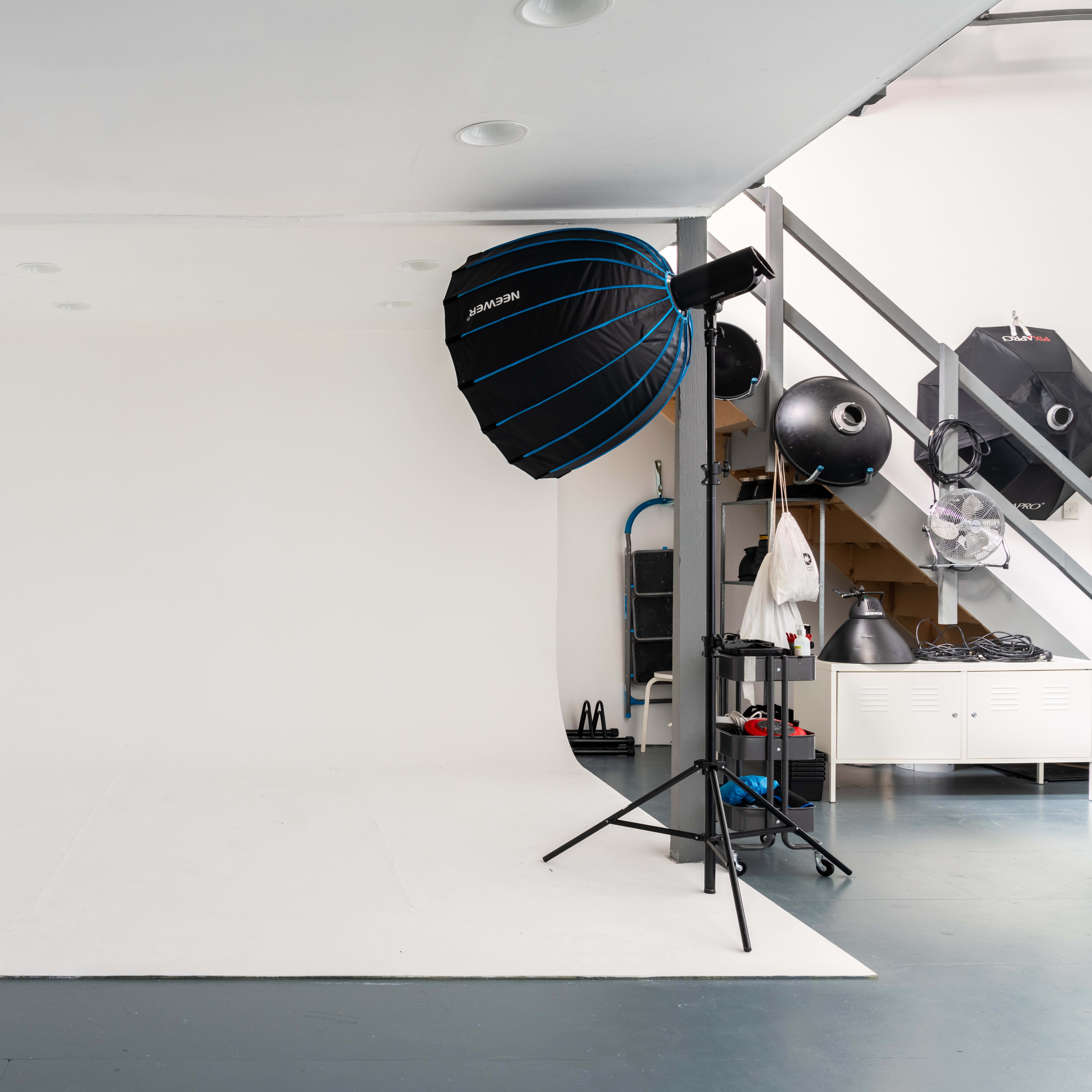 A photography studio featuring a seamless white backdrop, colorful paper rolls, and lighting equipment.