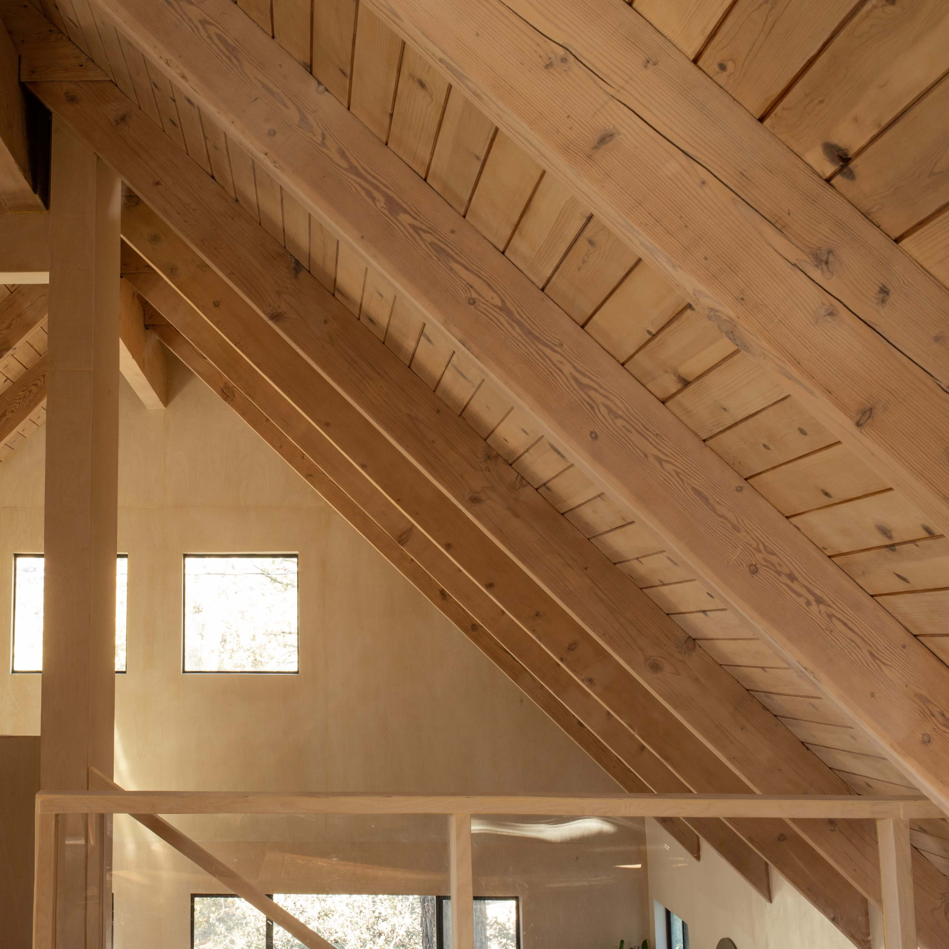 An interior space with exposed wooden beams and a sloped ceiling, featuring windows that allow natural light to enter.