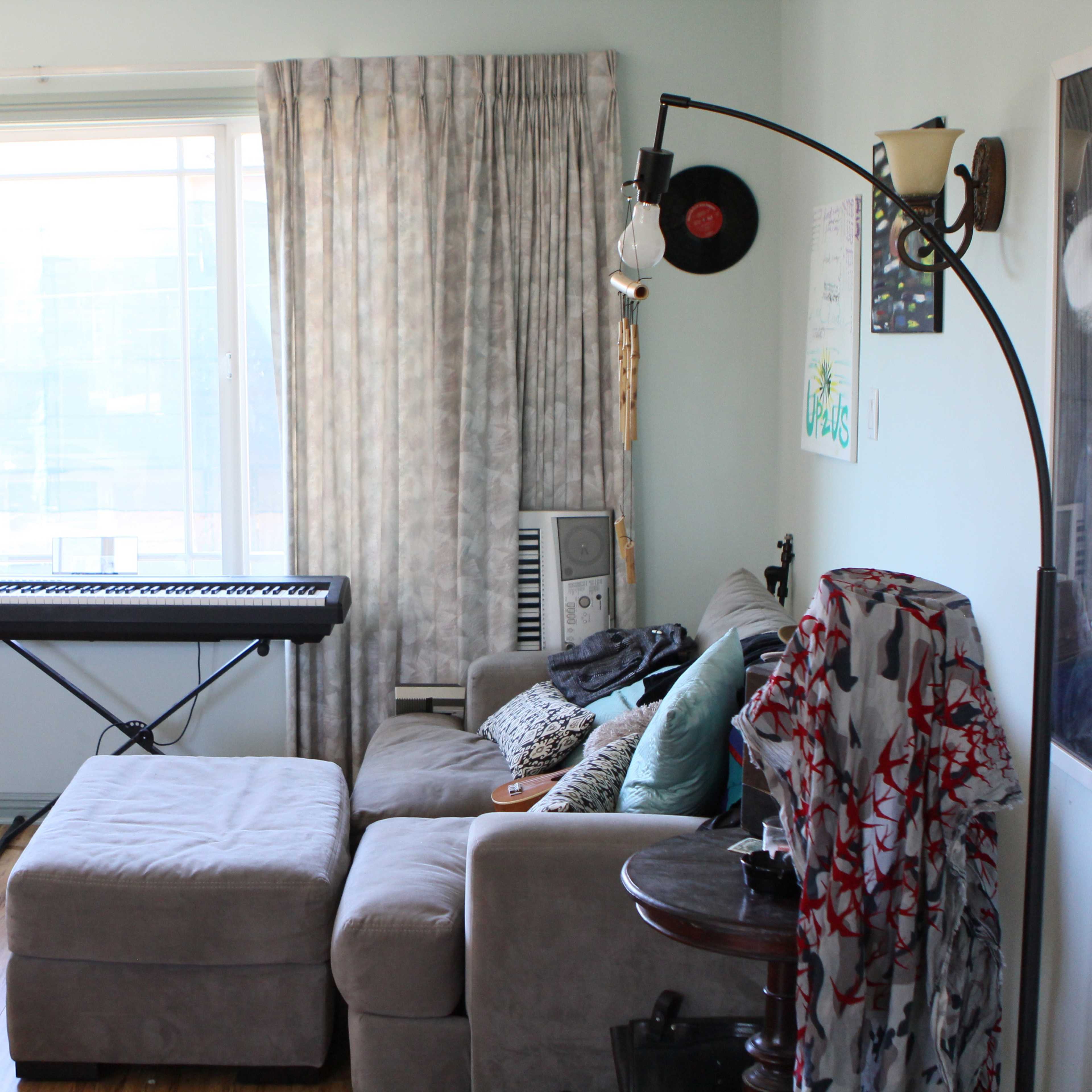 A living room features a keyboard, a guitar, a chair at a desk, and a couch with a throw blanket.