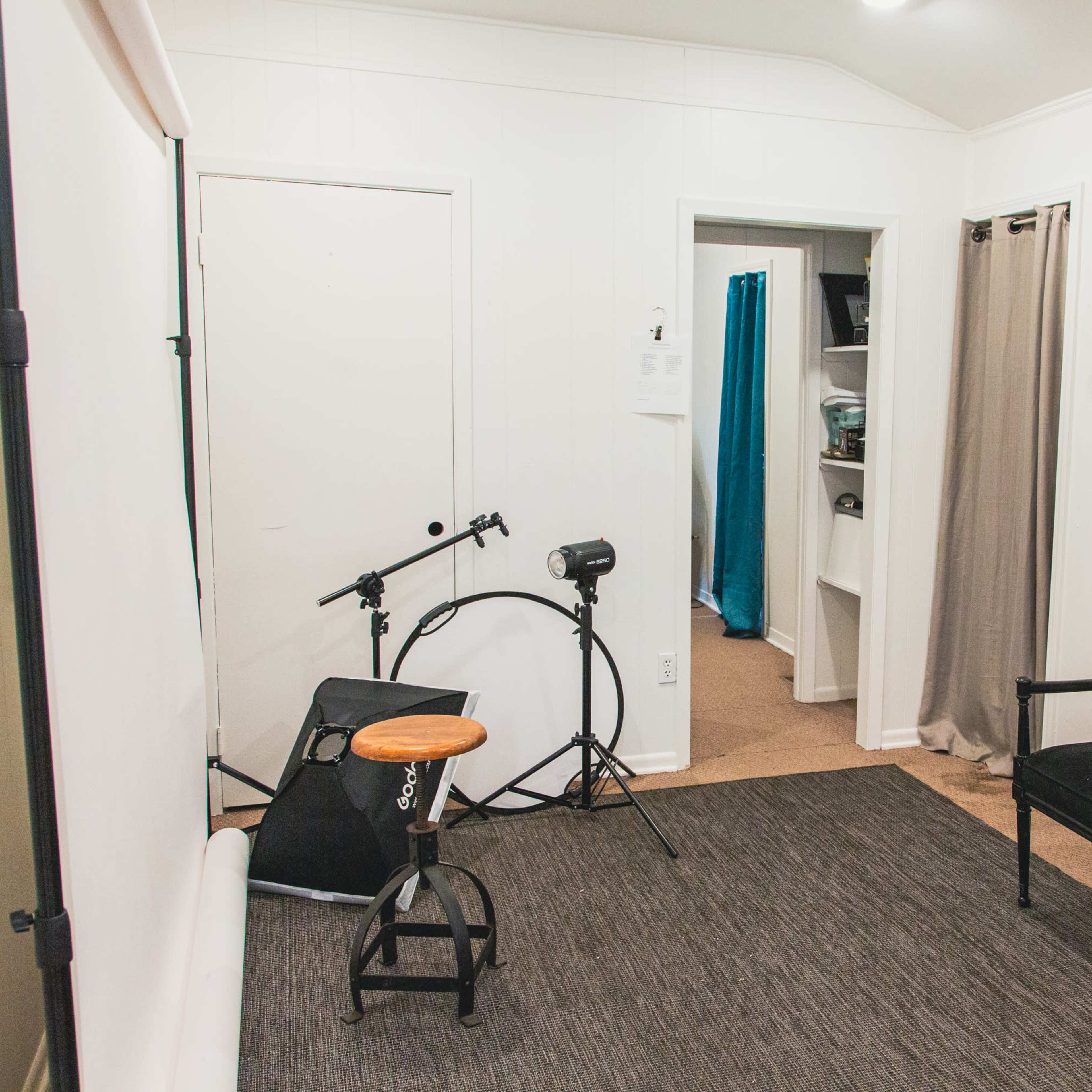 A small room features a chair, a drum kit, a stool, and curtains, with a doorway leading to another area.