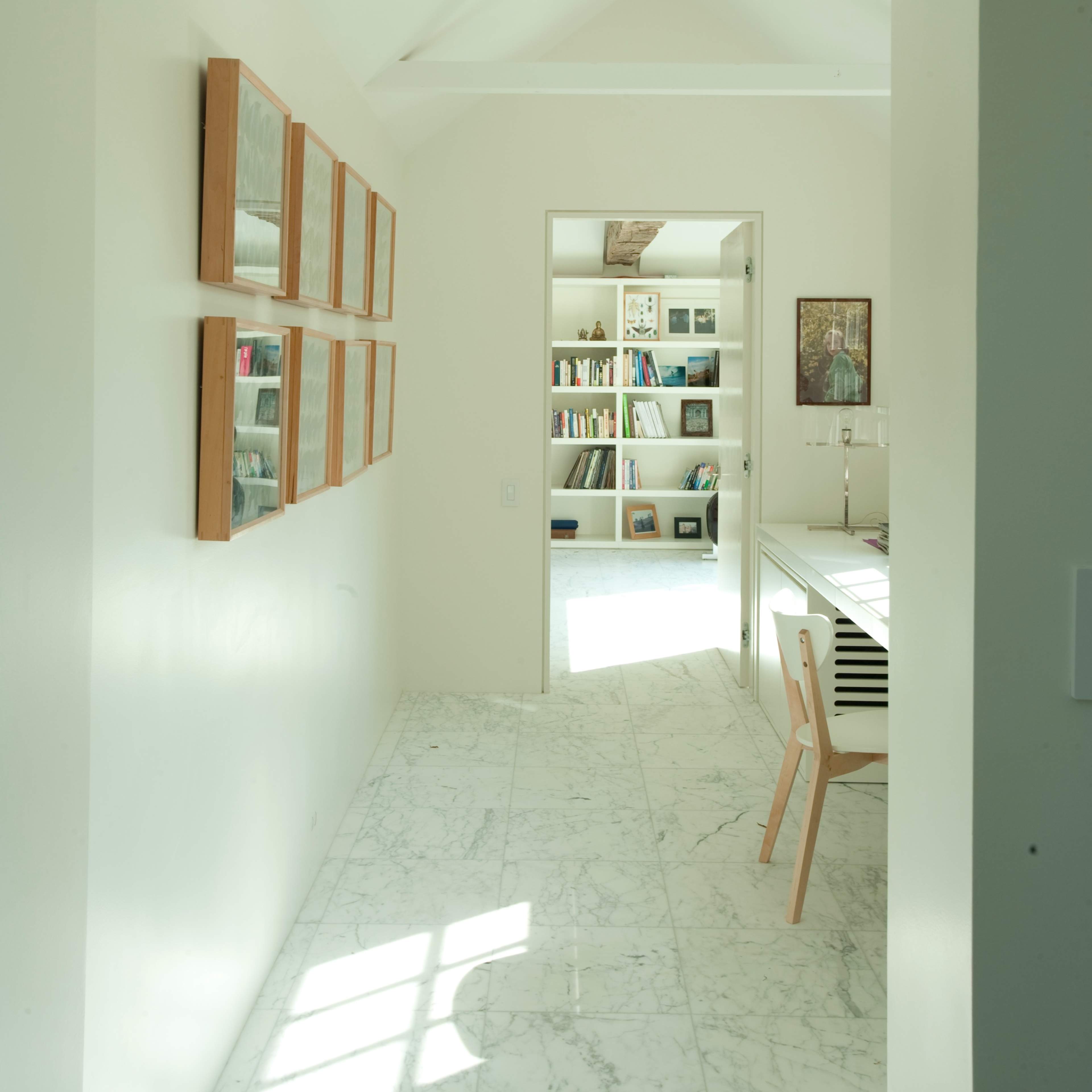 A bright, minimalistic hallway leading to a room filled with bookshelves and a desk.