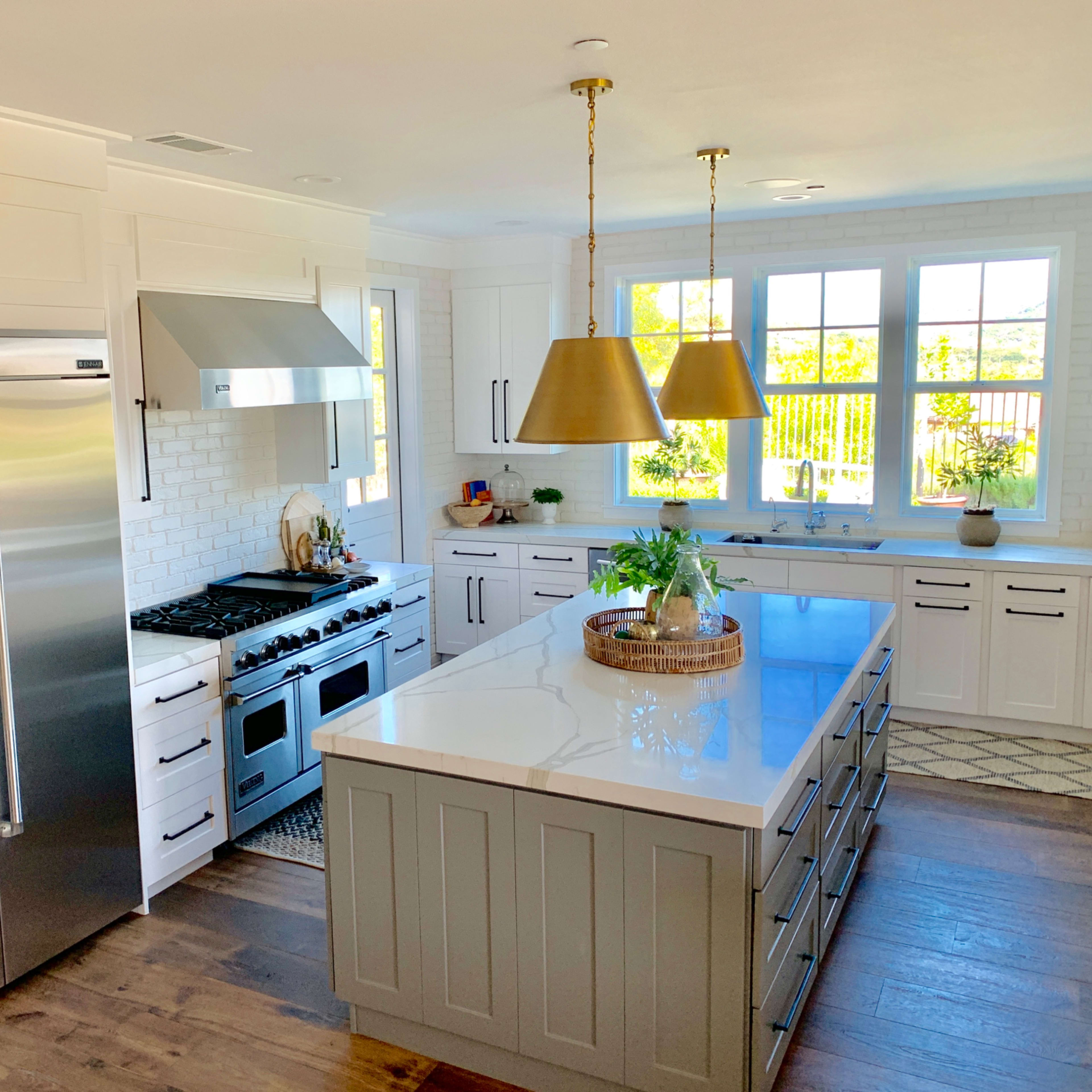 A modern kitchen features a large island with a white countertop, stainless steel appliances, and ample natural light from the windows.