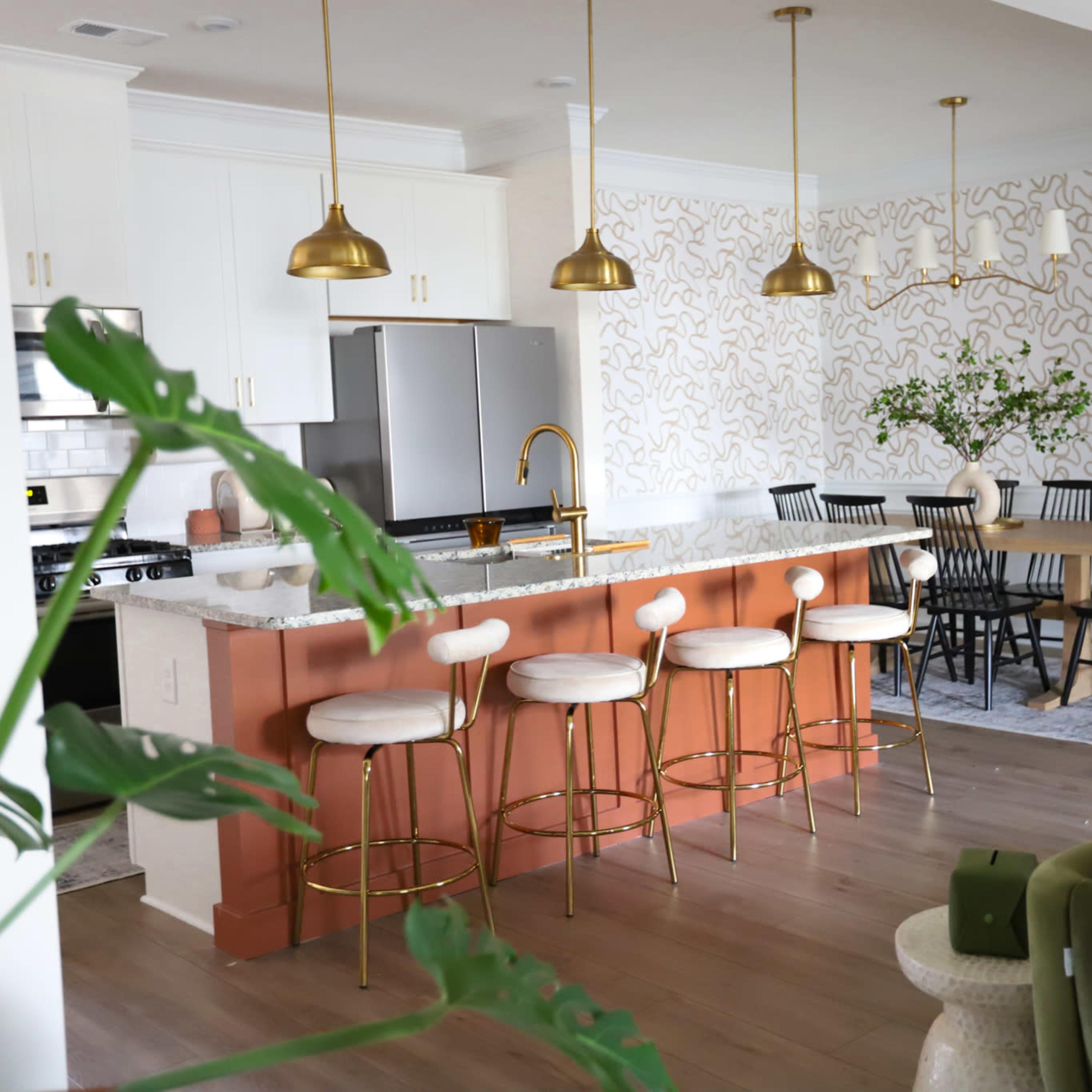A modern kitchen and dining area featuring a light color palette, with a central island bar, gold fixtures, and a dining table surrounded by black chairs.