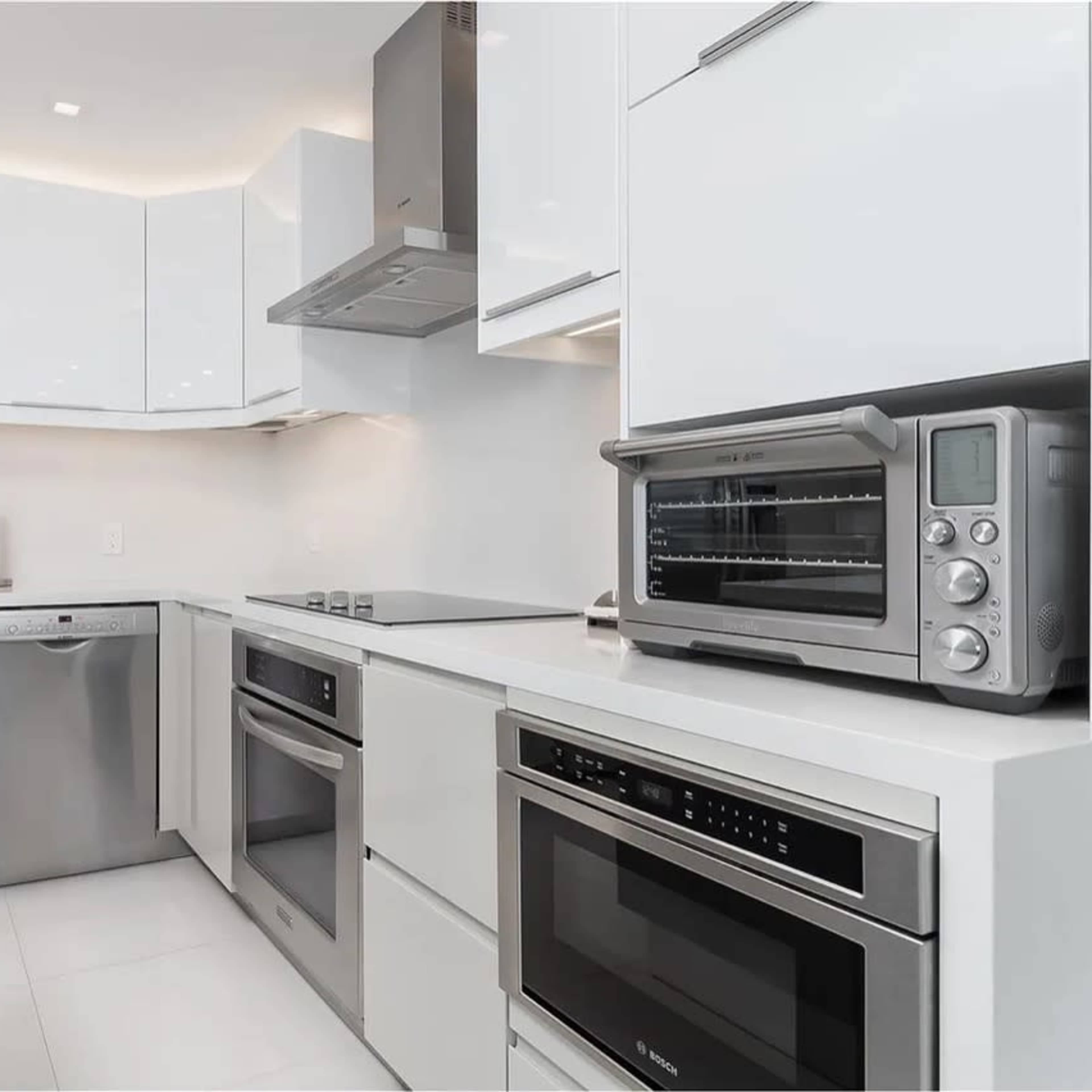 A modern kitchen equipped with stainless steel appliances, including a dishwasher, oven, and countertop toaster oven, set against sleek white cabinetry.