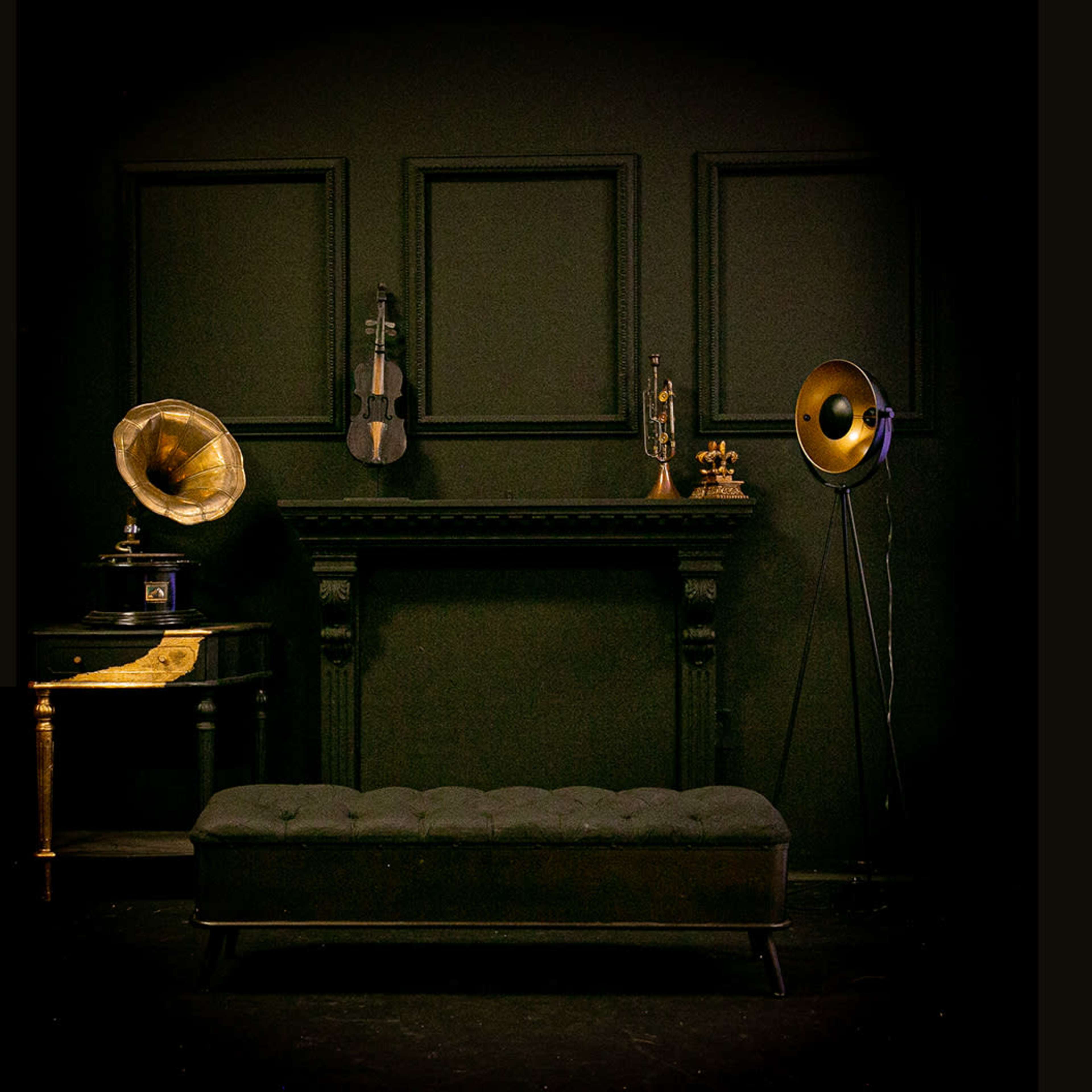 A black room with a tufted bench in front of a fireplace, surrounded by vintage musical instruments and decorative items.