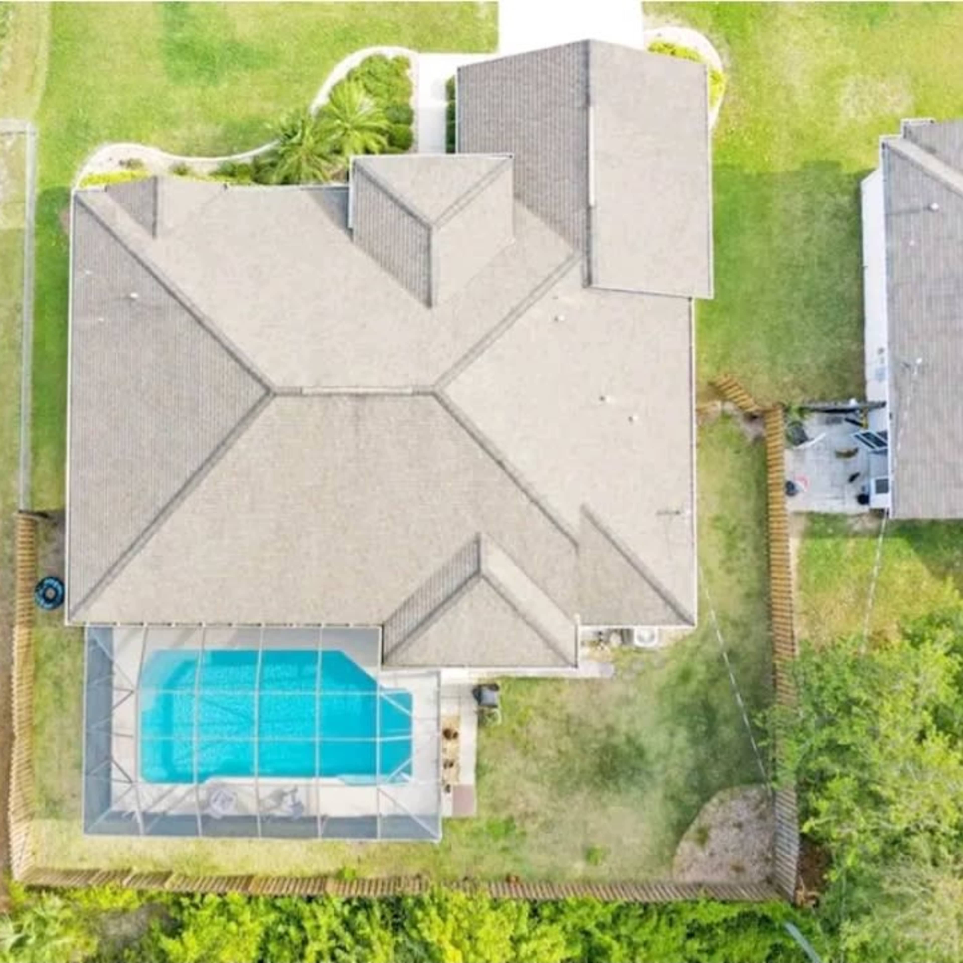 An aerial view shows a large house with a pool enclosed by a screen, surrounded by green grass and trees.