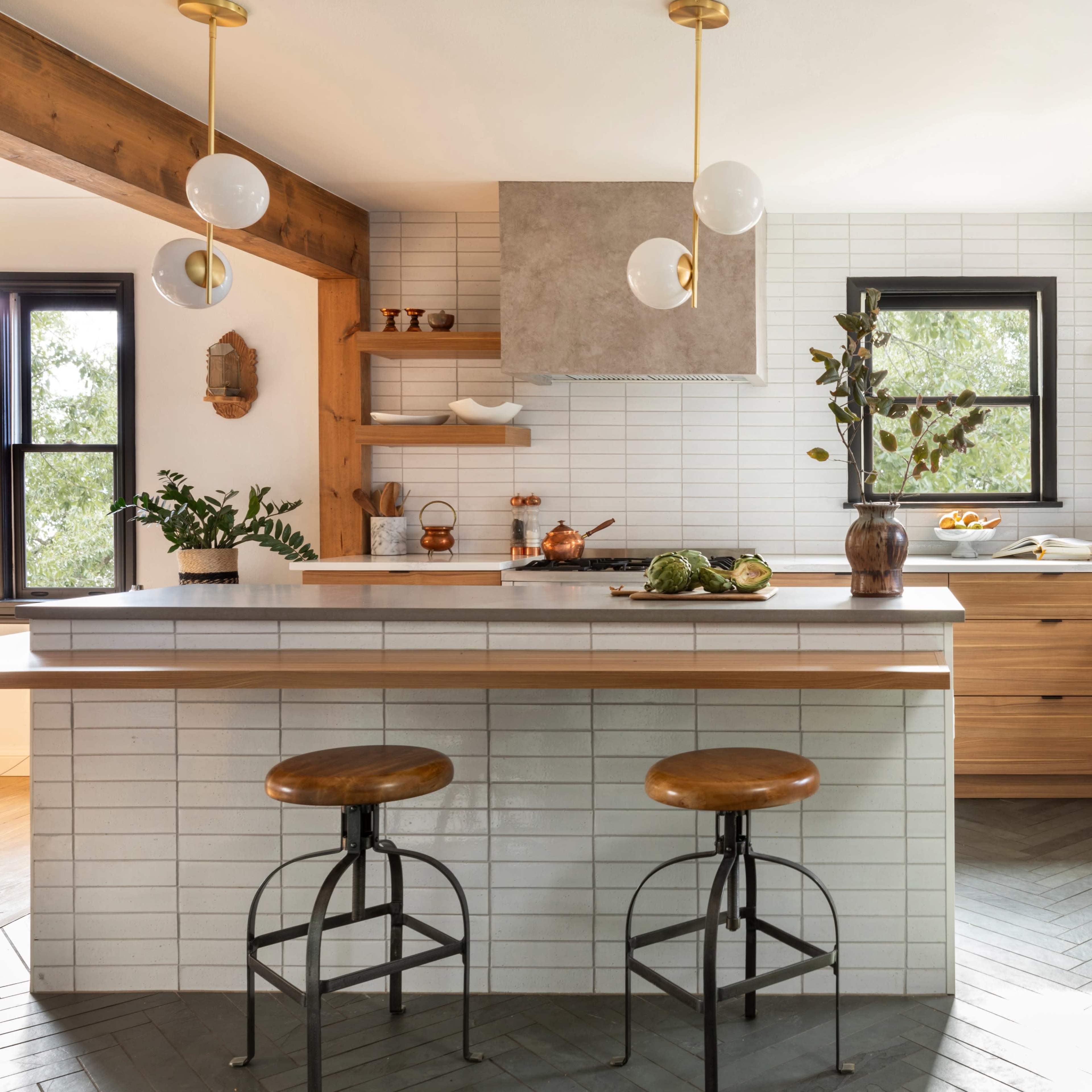 A modern kitchen features a wooden island with two stools, light-colored cabinetry, and open shelving filled with kitchenware.