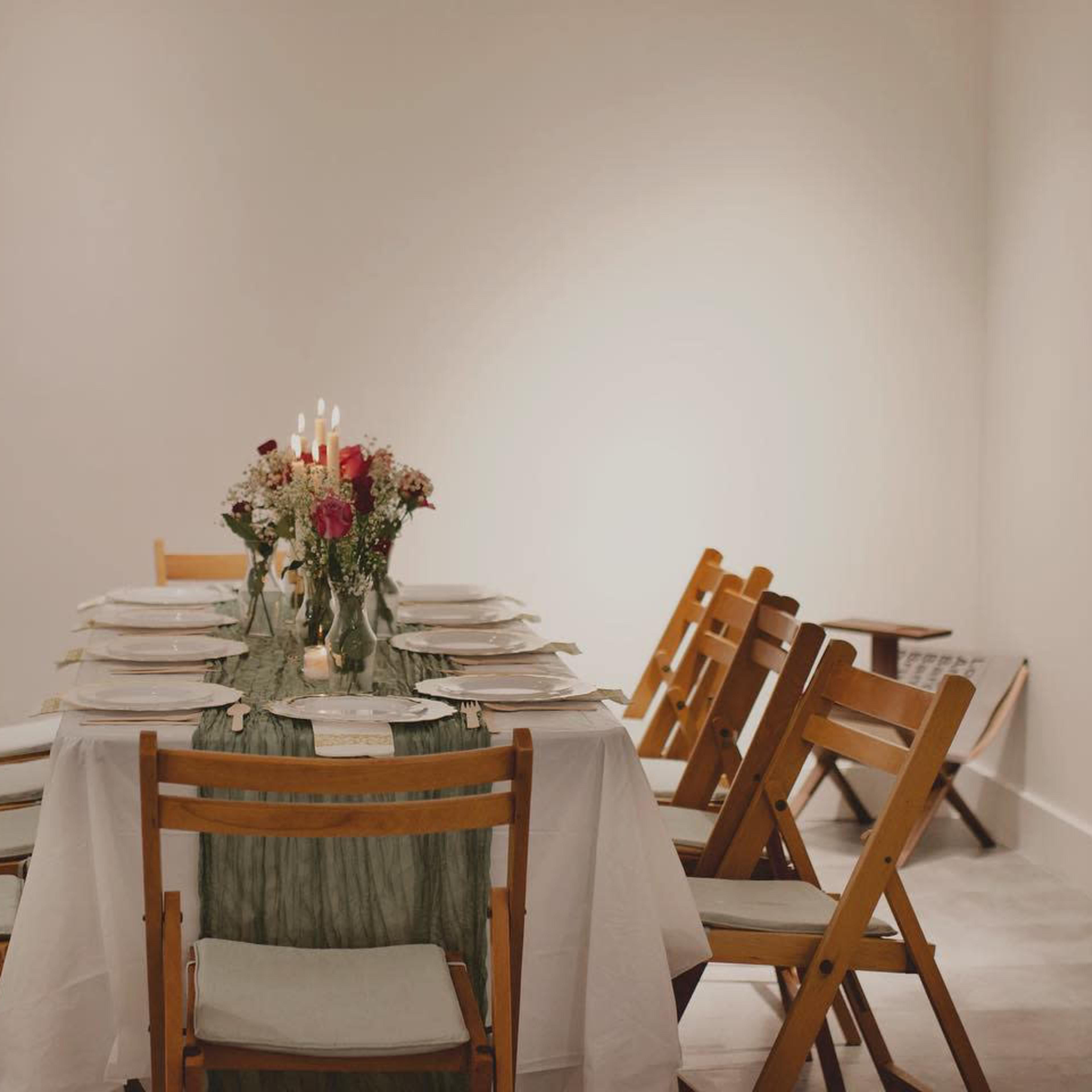 A long dining table is set with plates and a floral centerpiece, surrounded by wooden chairs in a softly lit room.