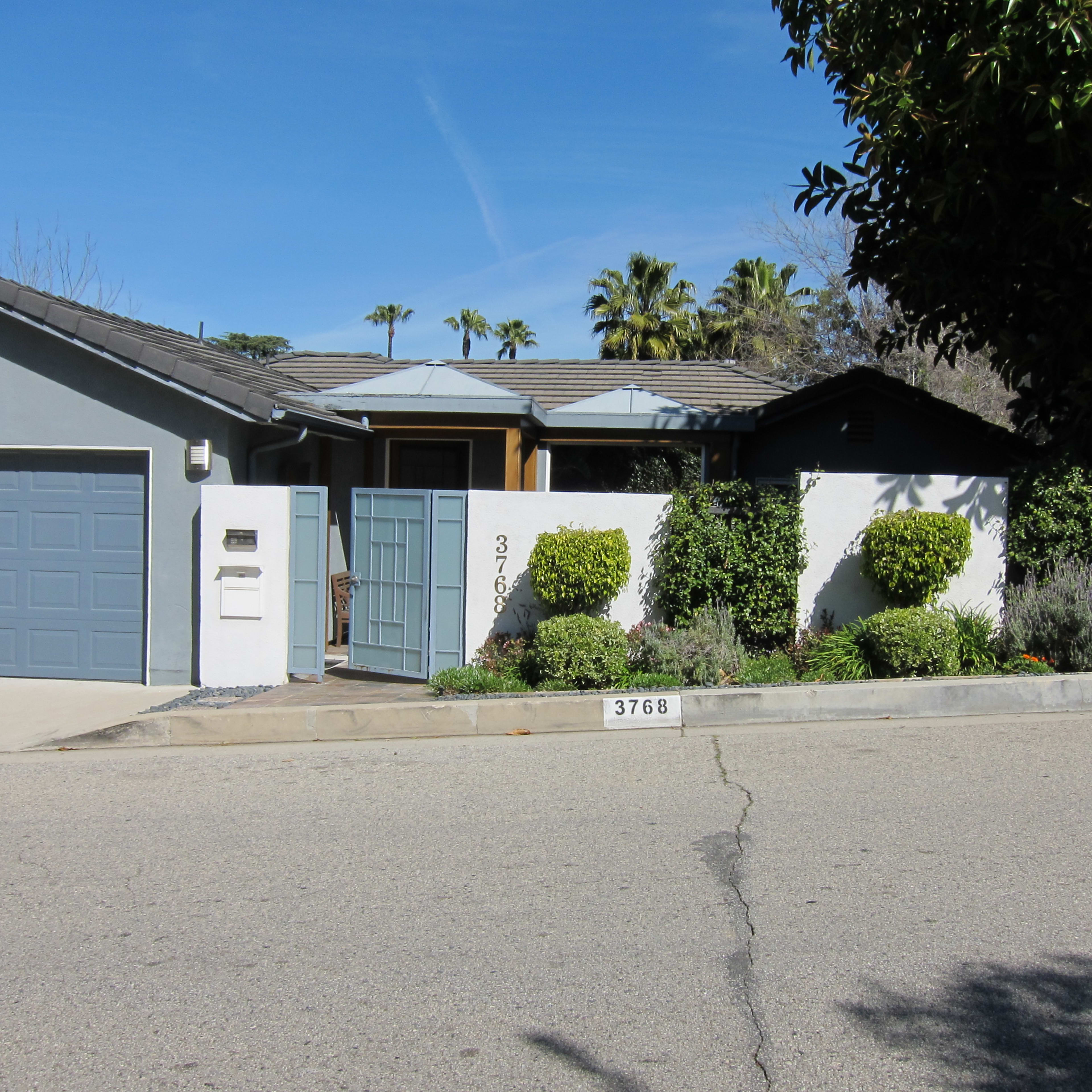 A single-story house with a gray garage door, a decorative front gate, and neatly trimmed landscaping along the sidewalk.