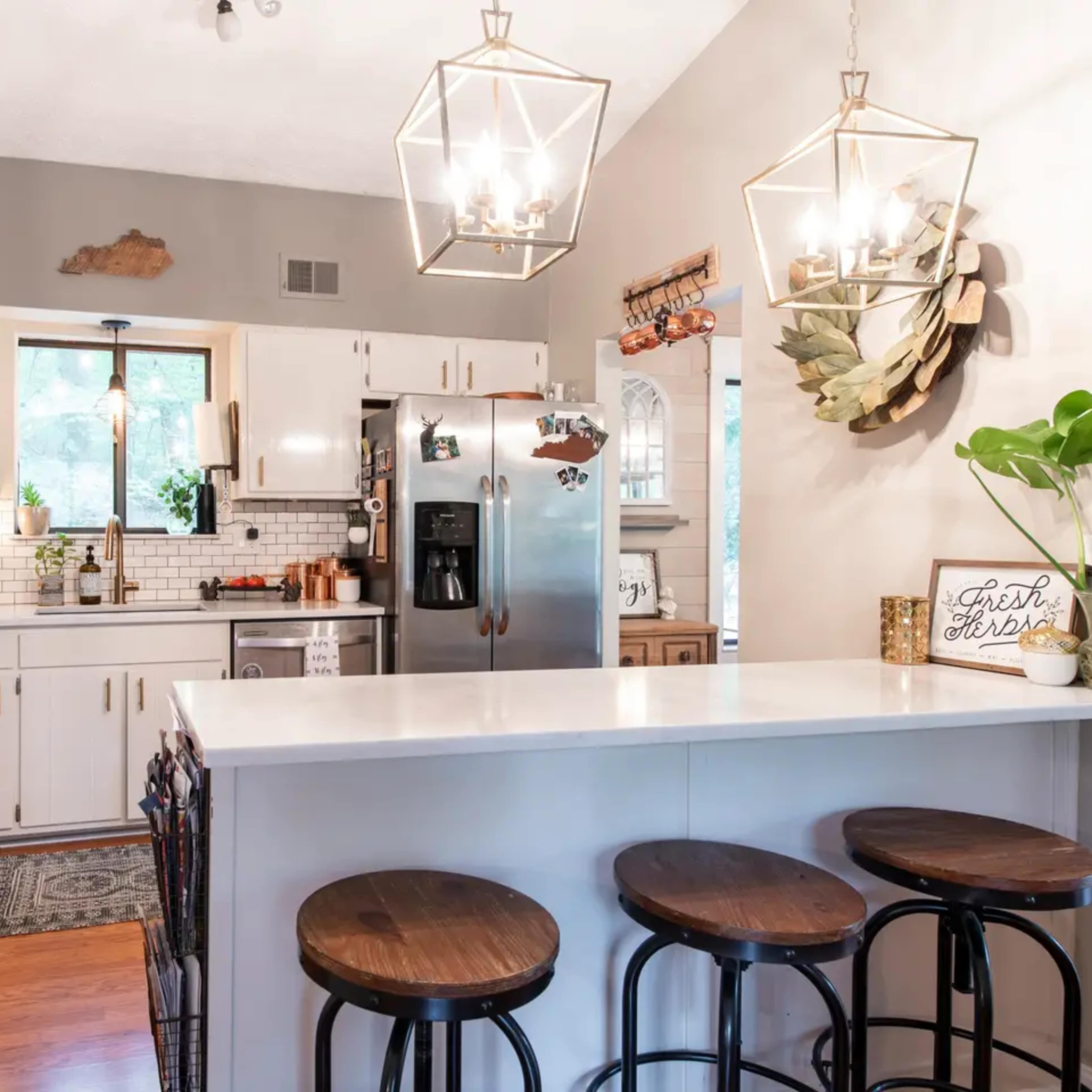 A modern kitchen with white cabinets, stainless steel appliances, and a central island featuring four wooden bar stools.