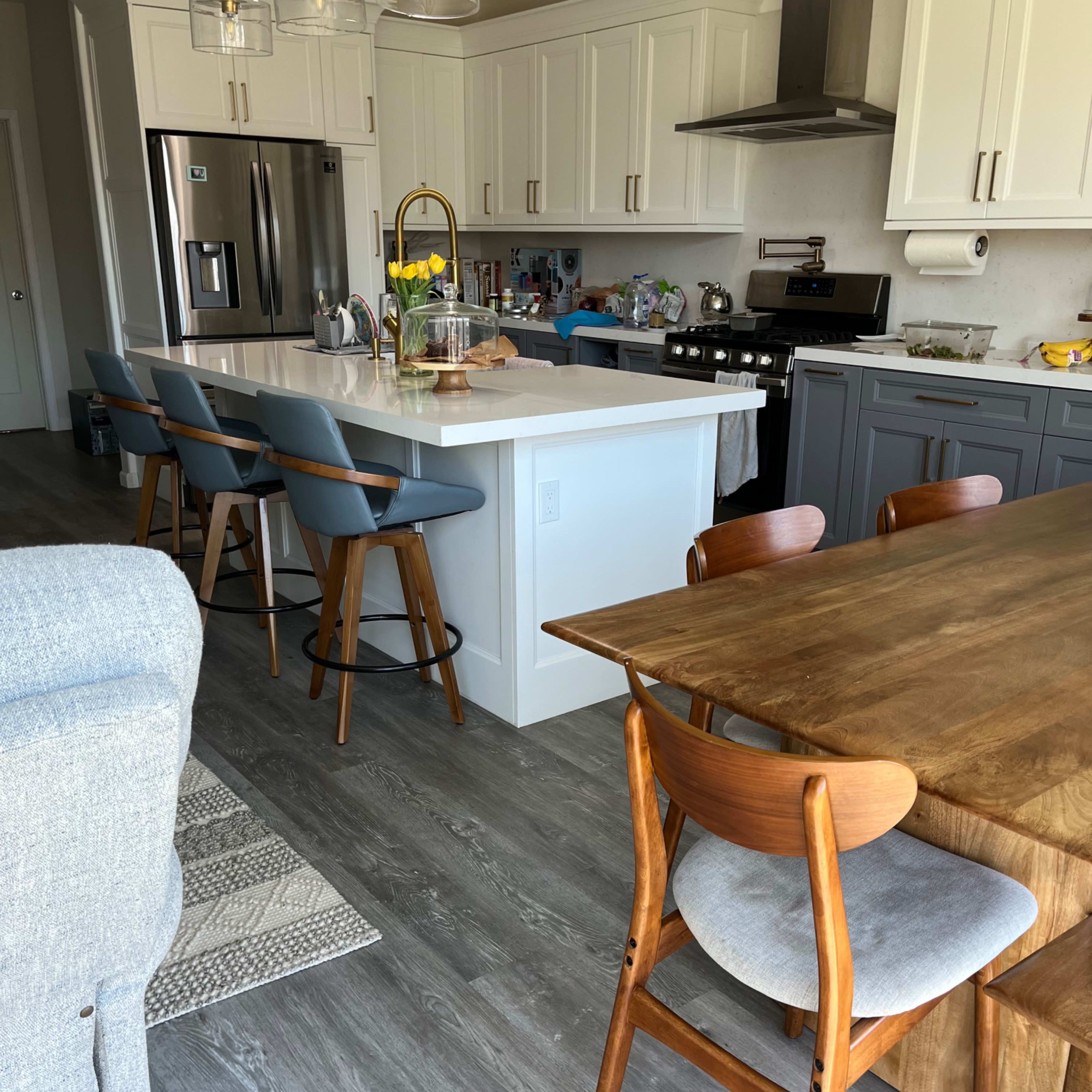 A modern kitchen featuring an island with stools, stainless steel appliances, and a wooden dining table.