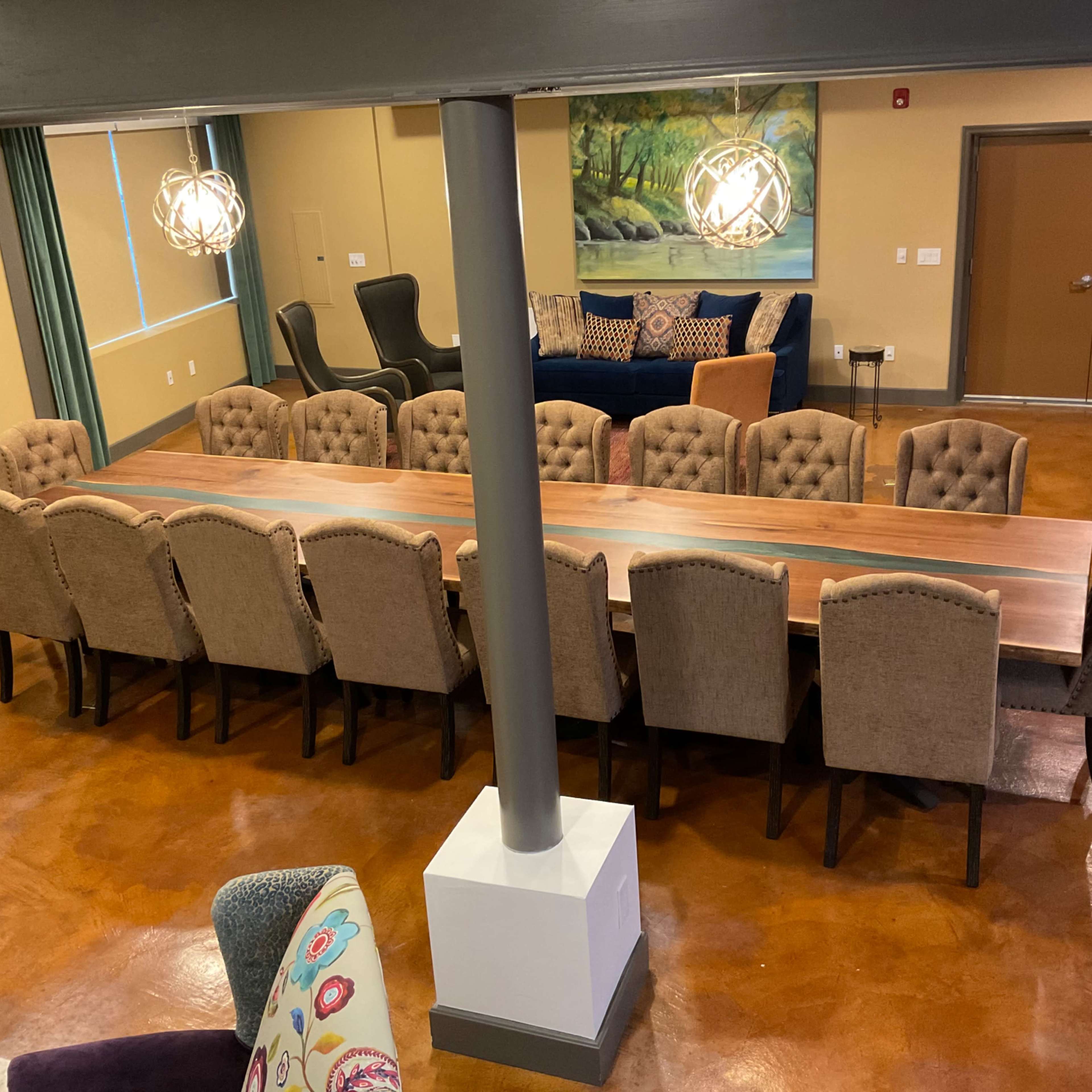 A large meeting room featuring a long wooden table surrounded by upholstered chairs, with a comfortable seating area in the background.