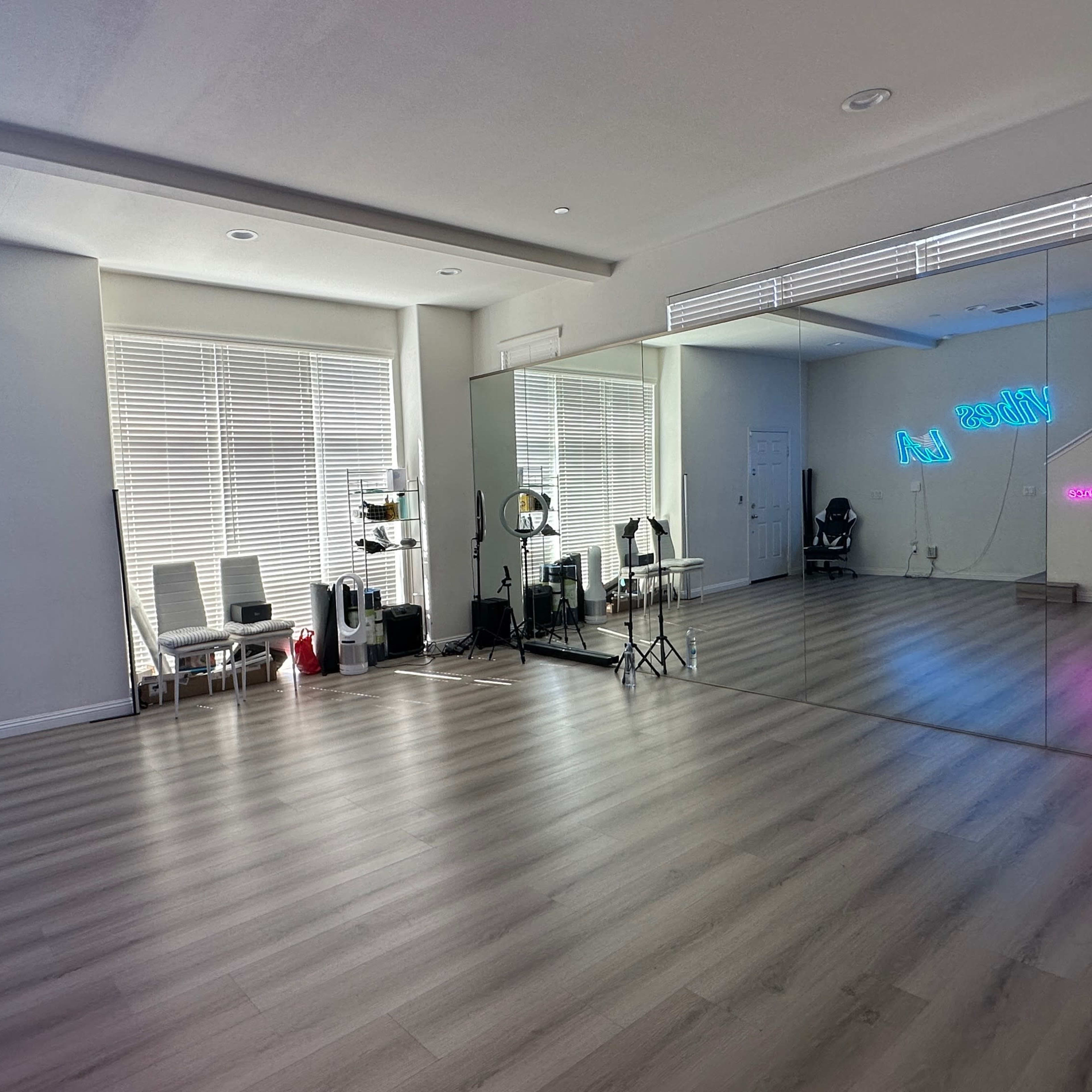 A spacious, well-lit studio with large windows, a mirrored wall, and several chairs arranged along one side.