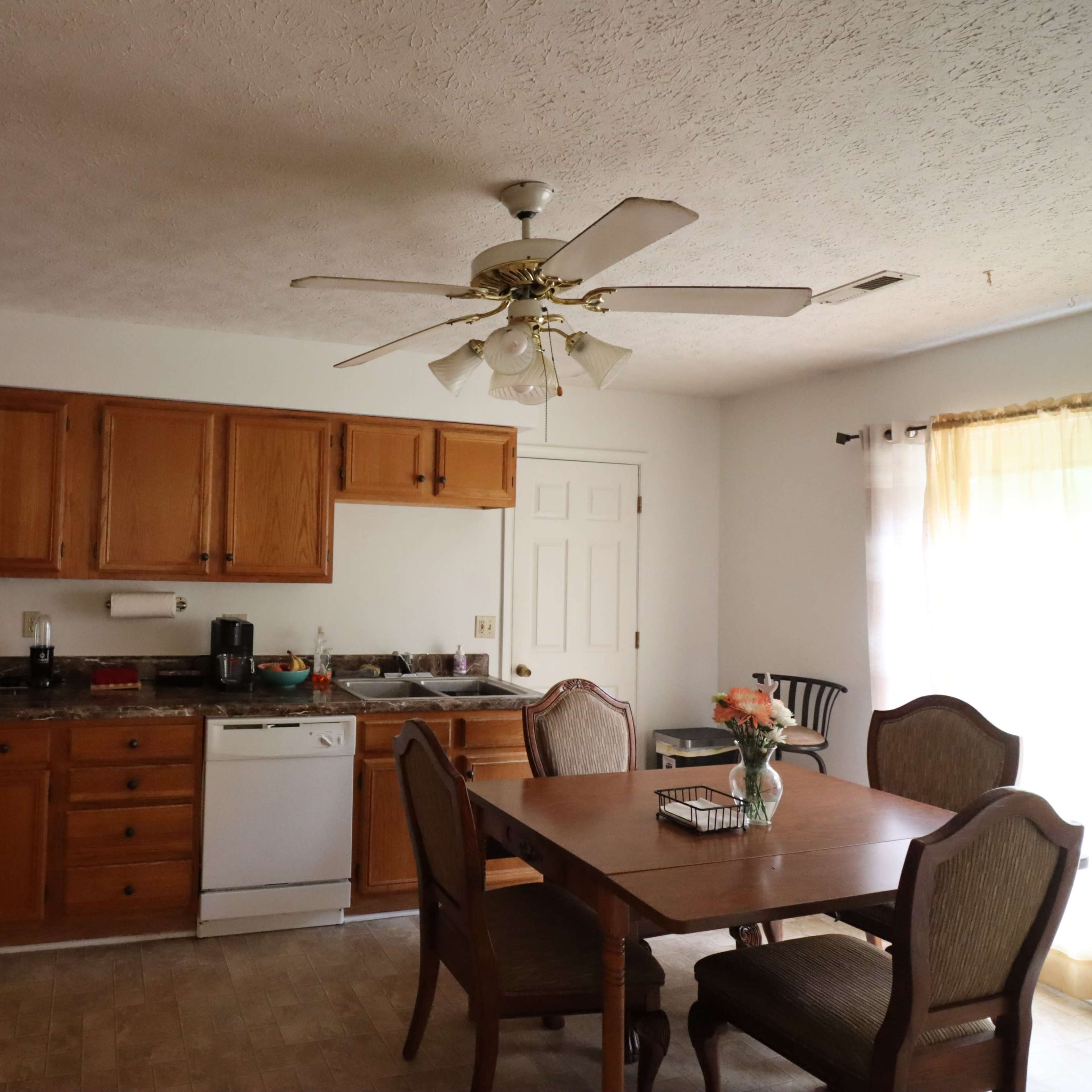 A kitchen features wooden cabinets, a dishwasher, and a dining table with chairs in a well-lit space.