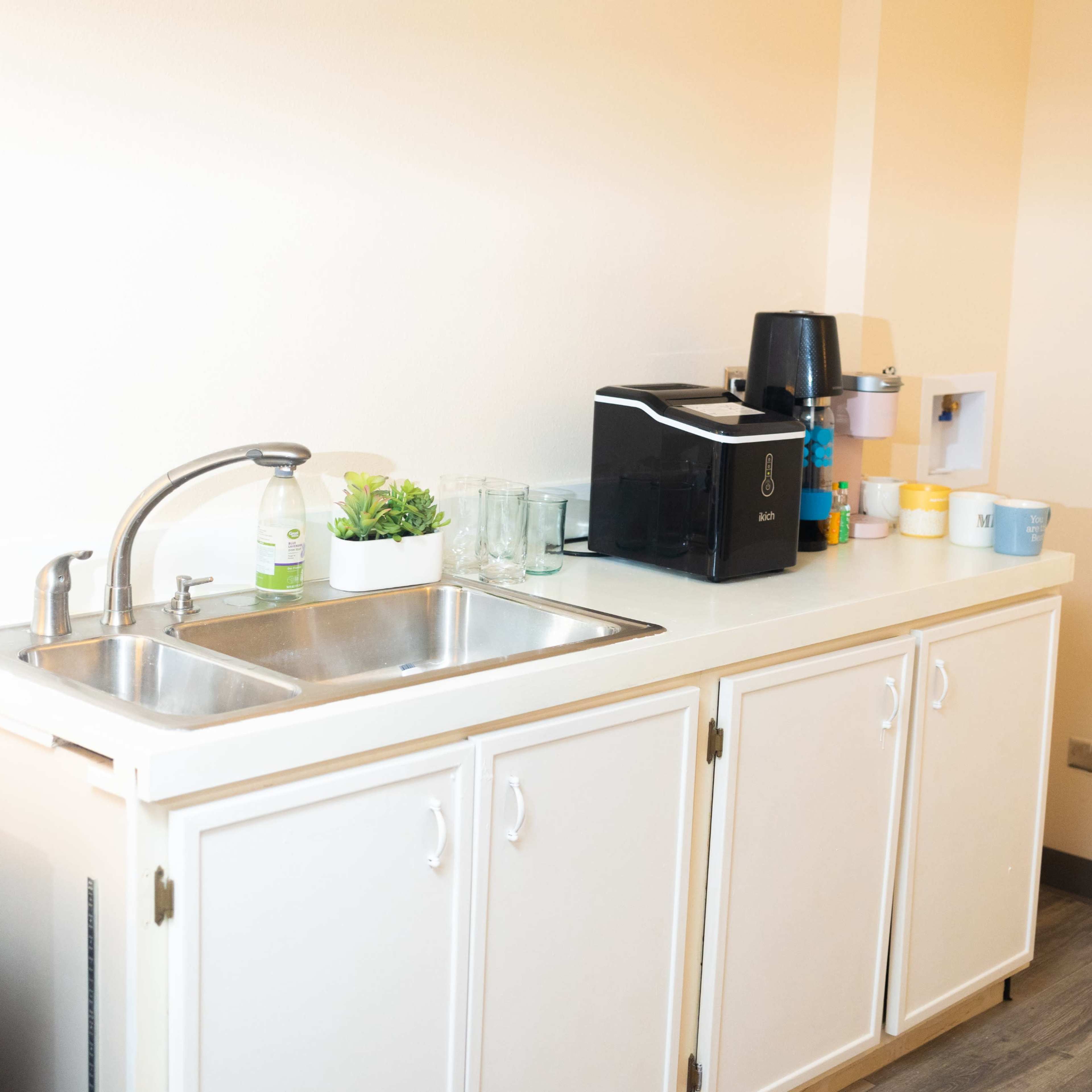 A kitchen area featuring a double sink, a coffee maker, and various cups on a countertop.