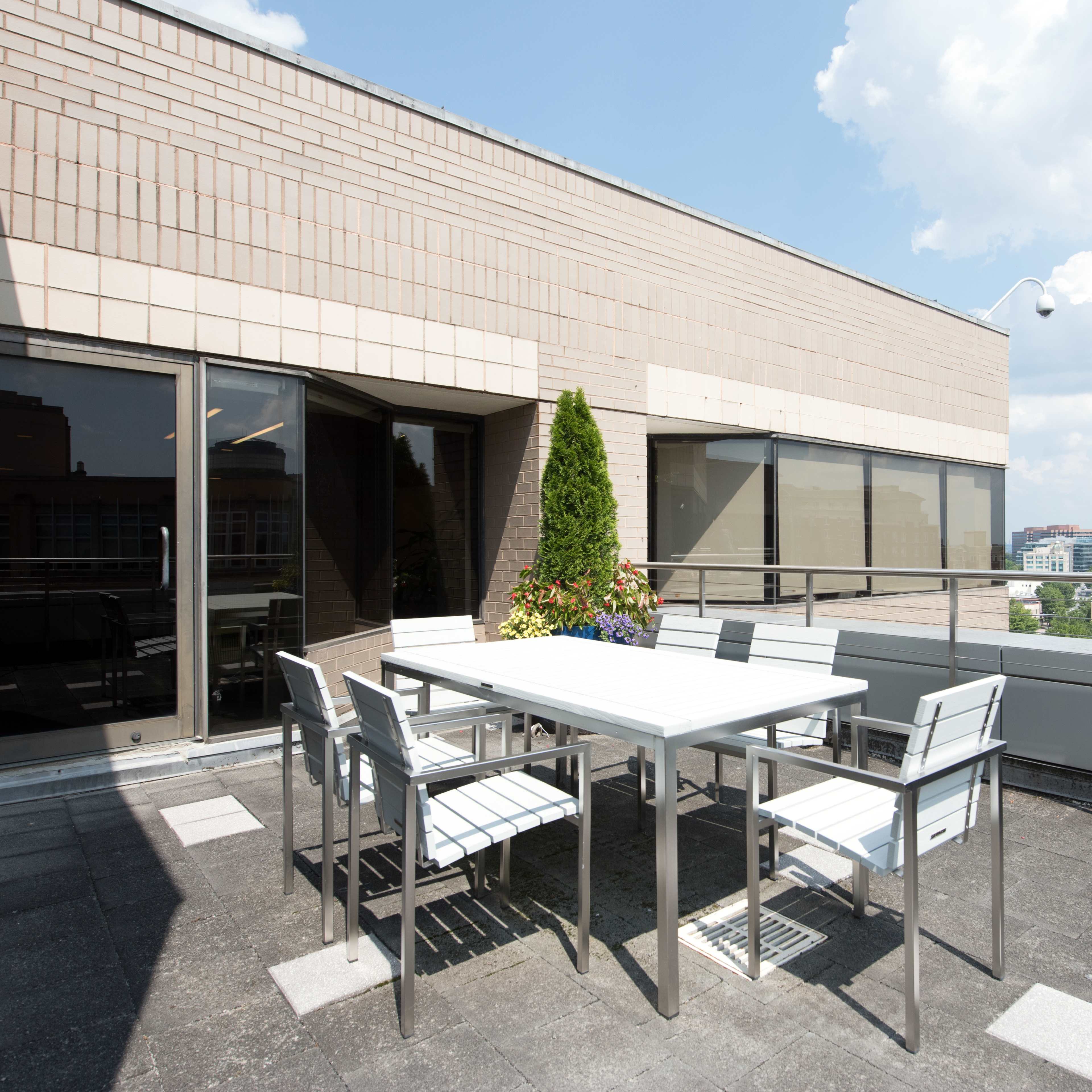 A rooftop terrace features a white dining table surrounded by chairs, with city buildings visible in the background.