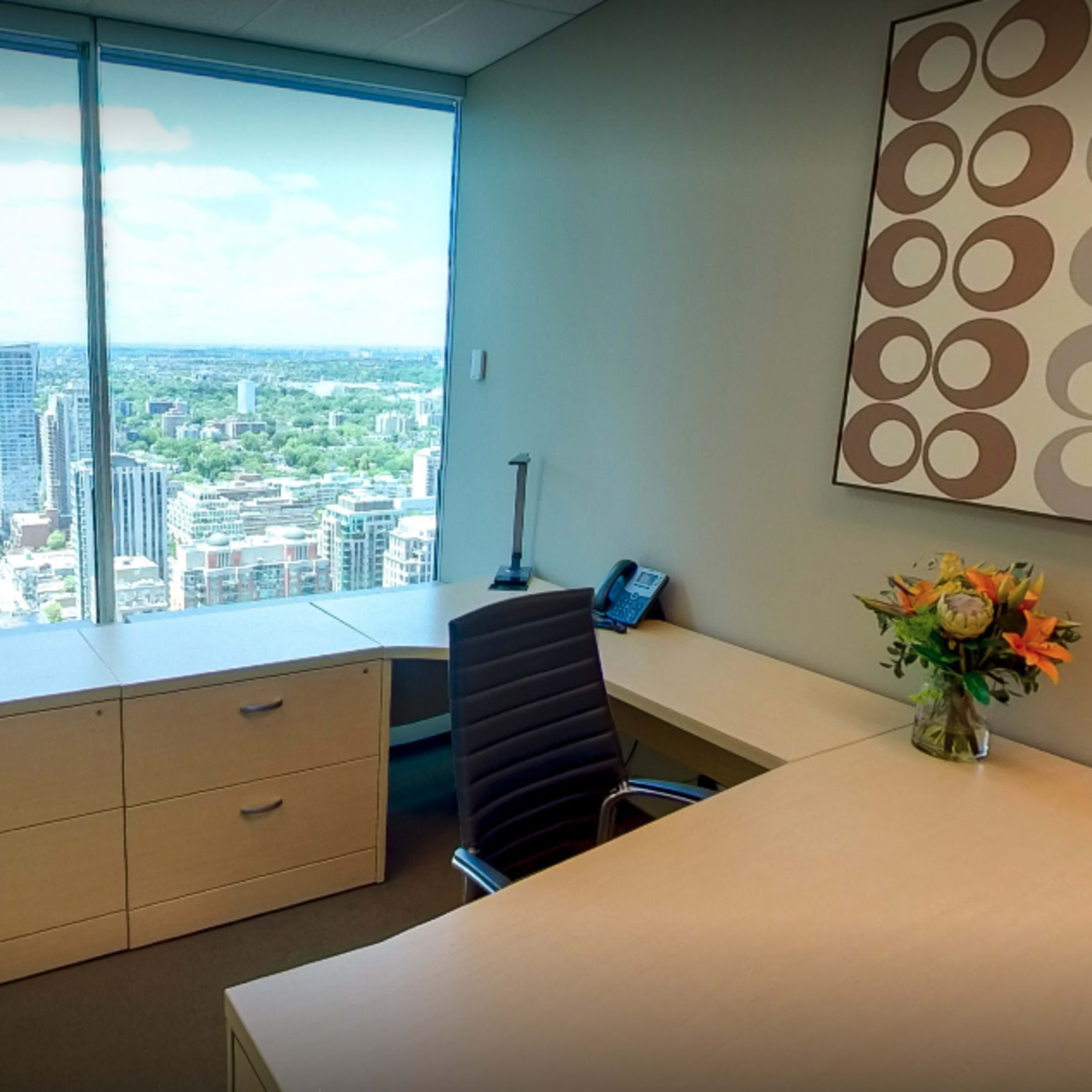 A modern office space with a desk, a chair, and large windows showcasing a cityscape view.