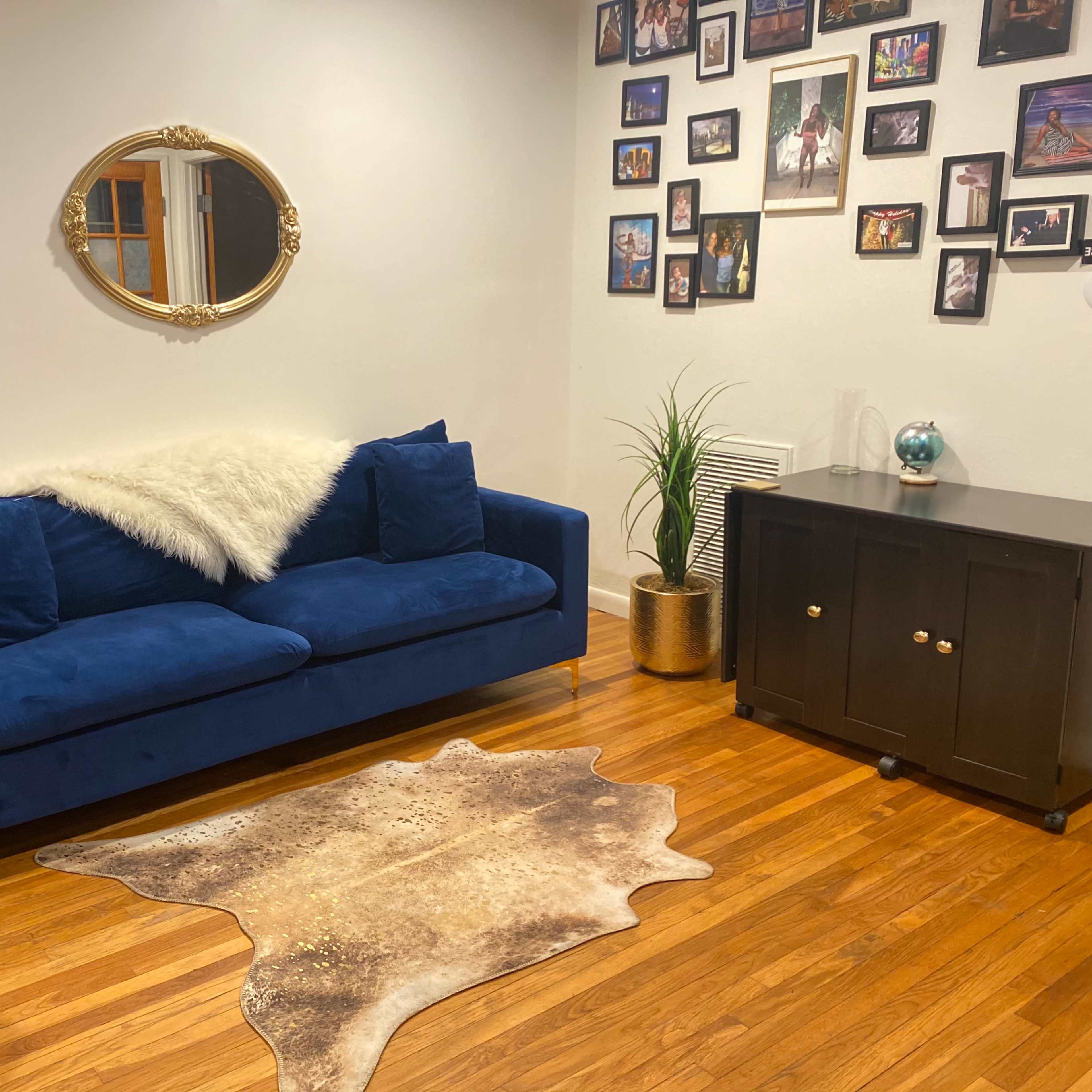 A cozy living area featuring a blue sofa with a white throw blanket, a cowhide rug on the wooden floor, and a wall adorned with framed photos.