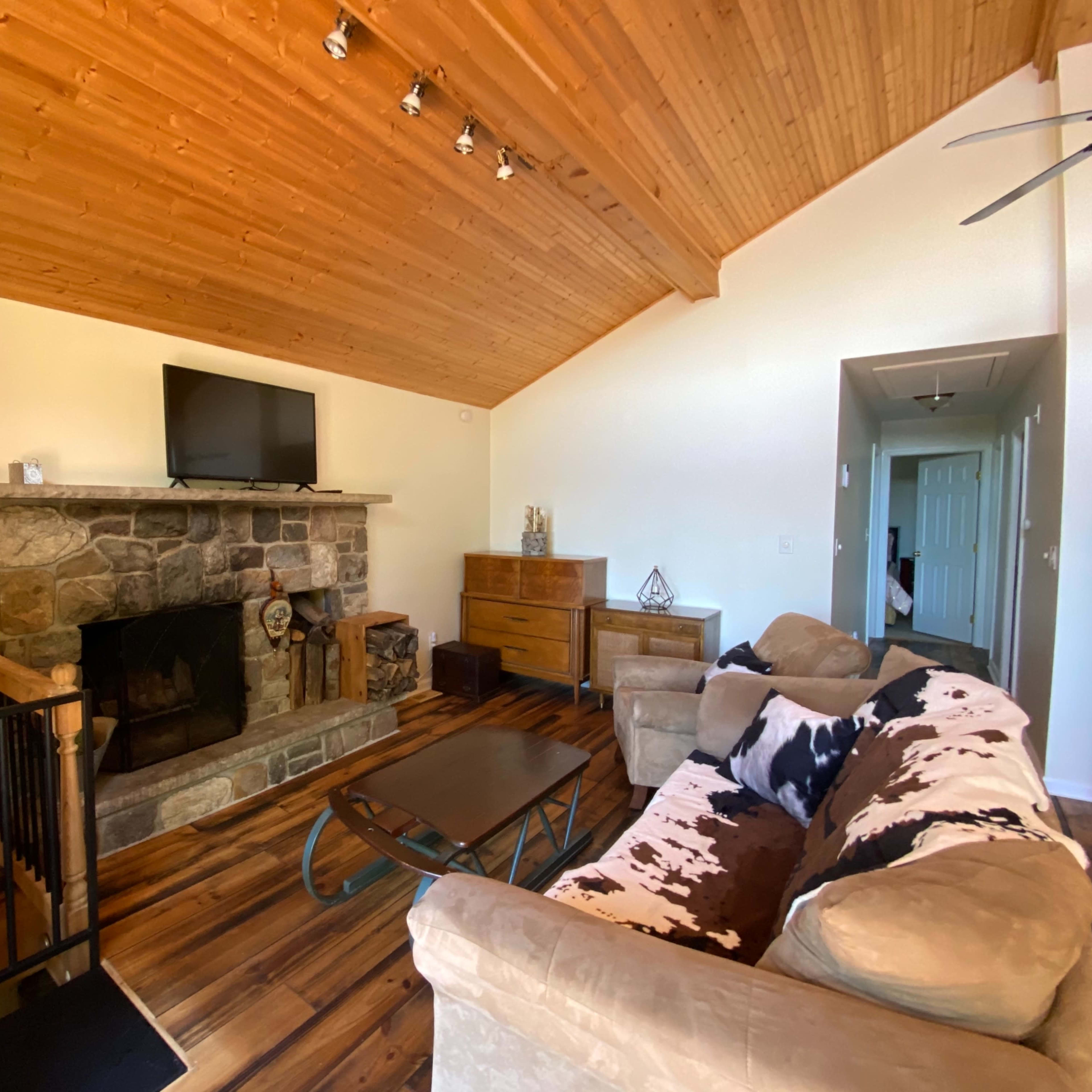 A living room with a stone fireplace, wooden ceiling, and a sofa facing a coffee table.