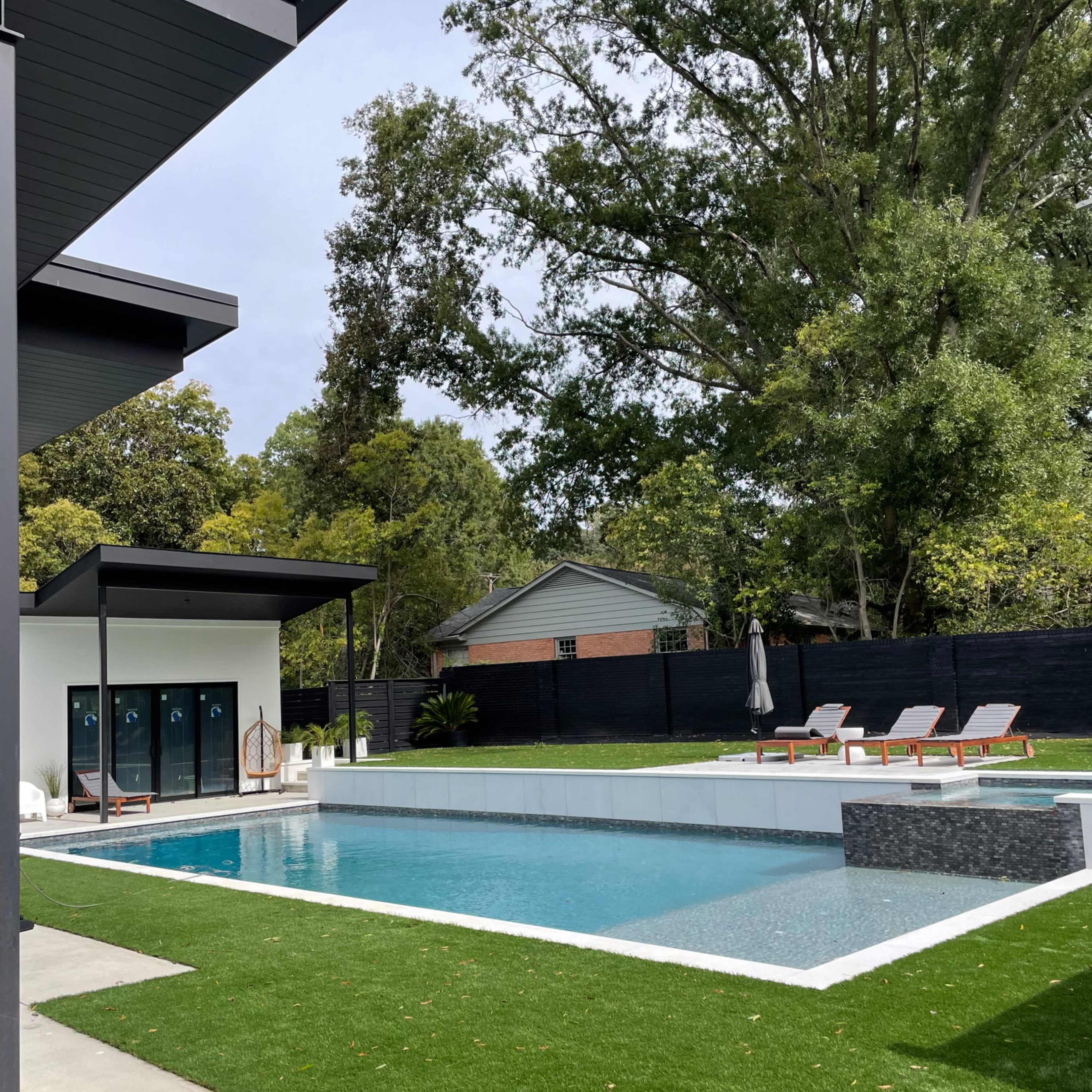 A modern backyard with a swimming pool, lounge chairs, and a nearby changing area.
