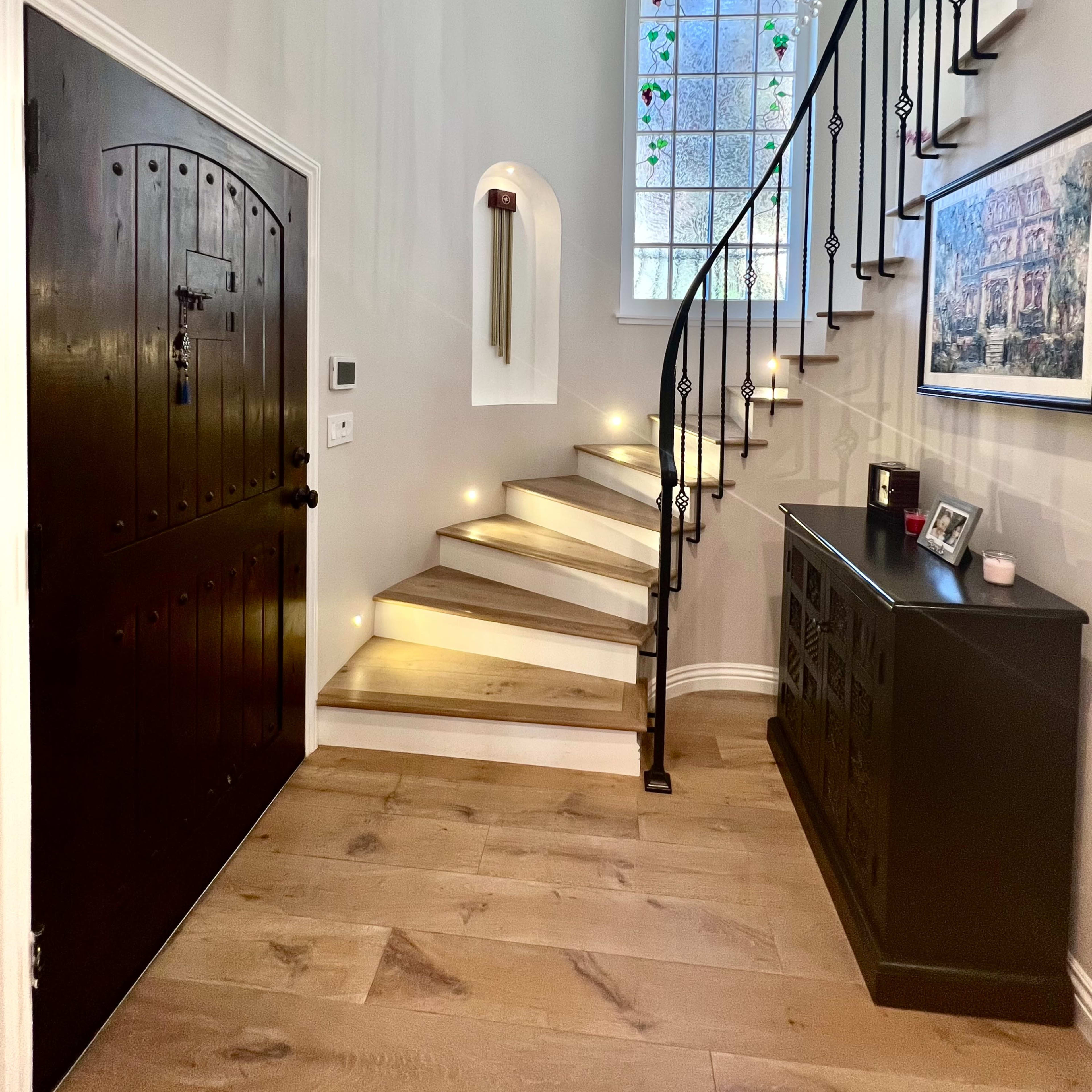 A stairway with illuminated steps leading up to a stained glass window in a well-furnished entryway.