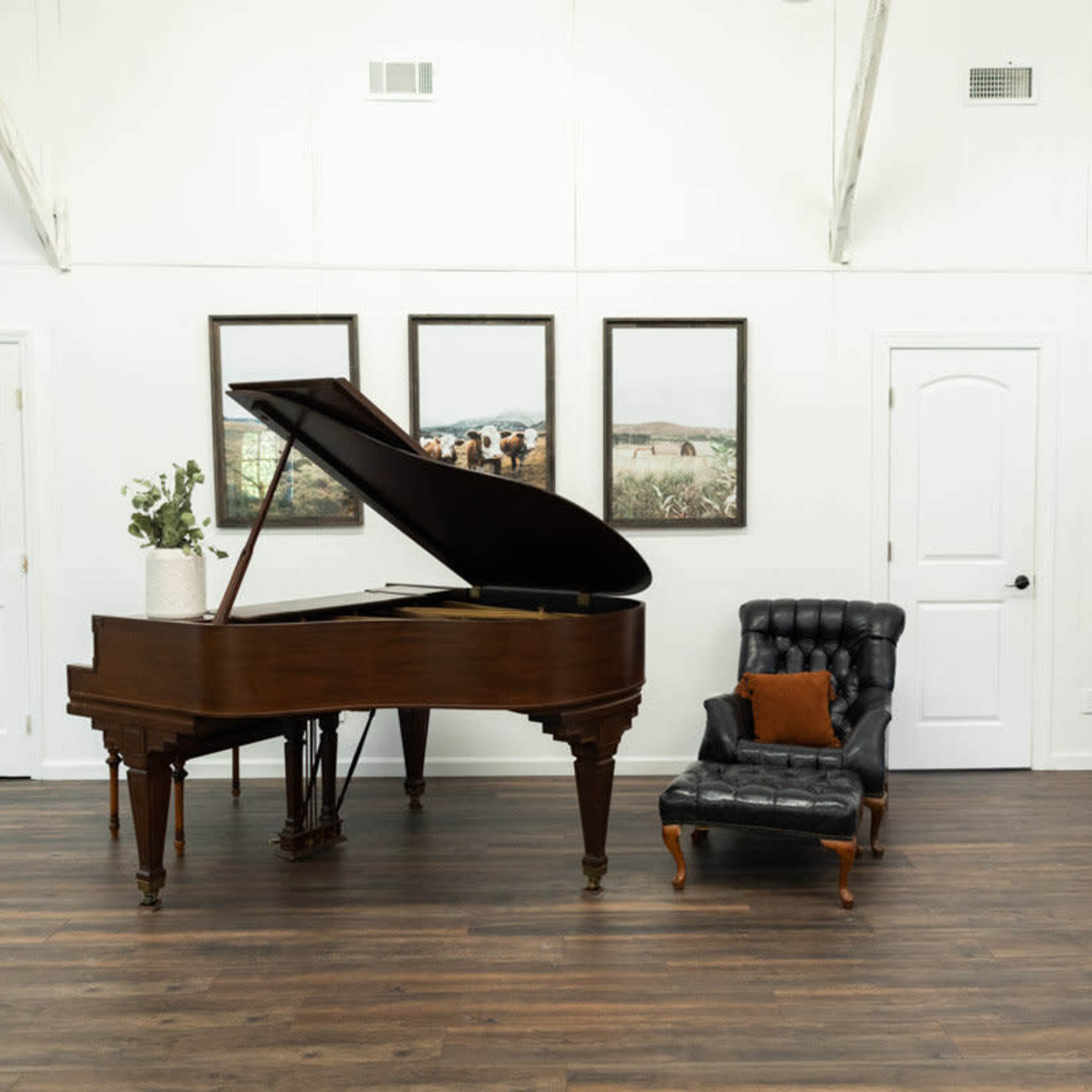 A grand piano sits next to a tufted armchair in a bright, open room with white walls and wooden flooring.