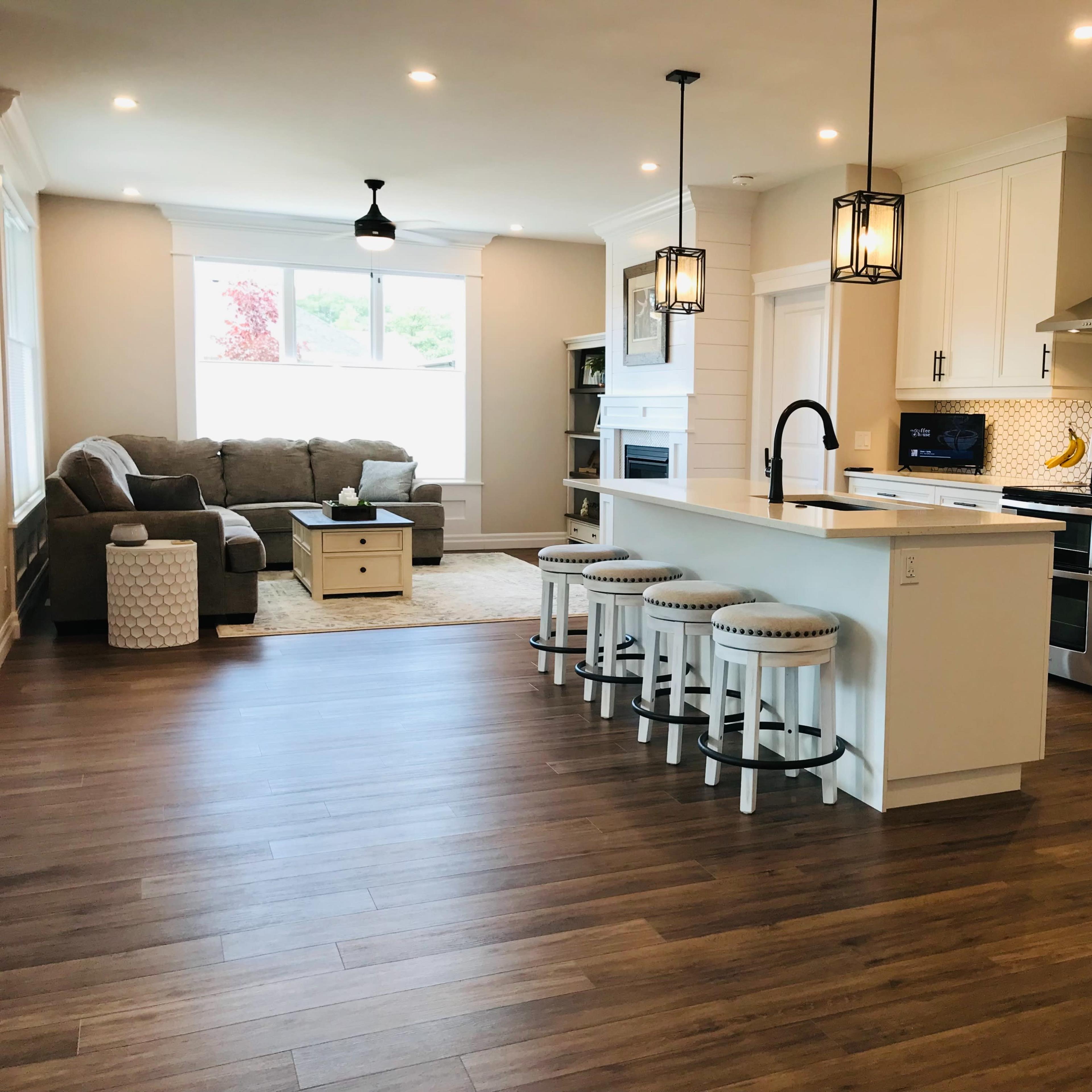 A modern kitchen and living area with white cabinetry, a large island with seating, and a gray sofa beside a window.