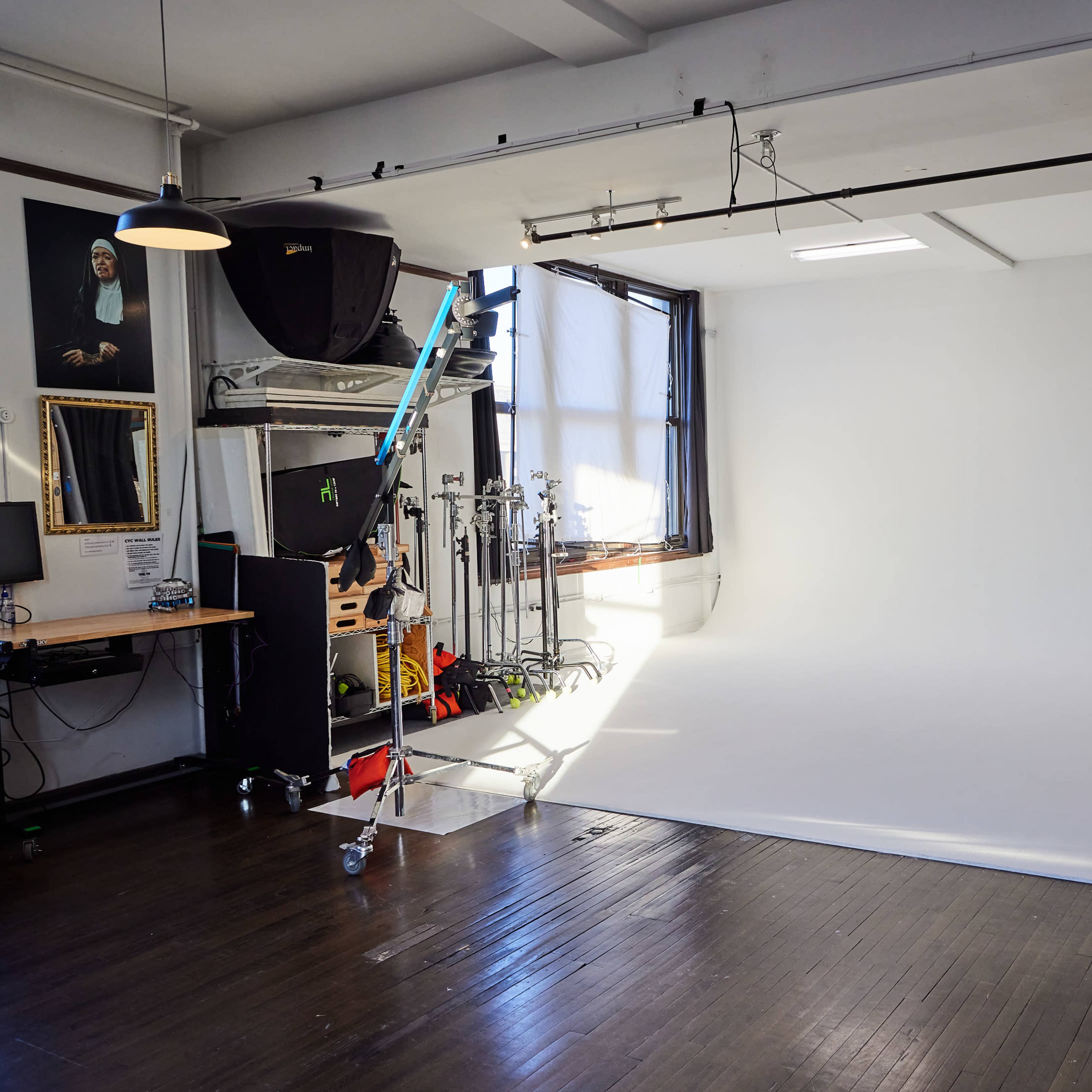 A photography studio with a white backdrop, lighting equipment, and a large window providing natural light.