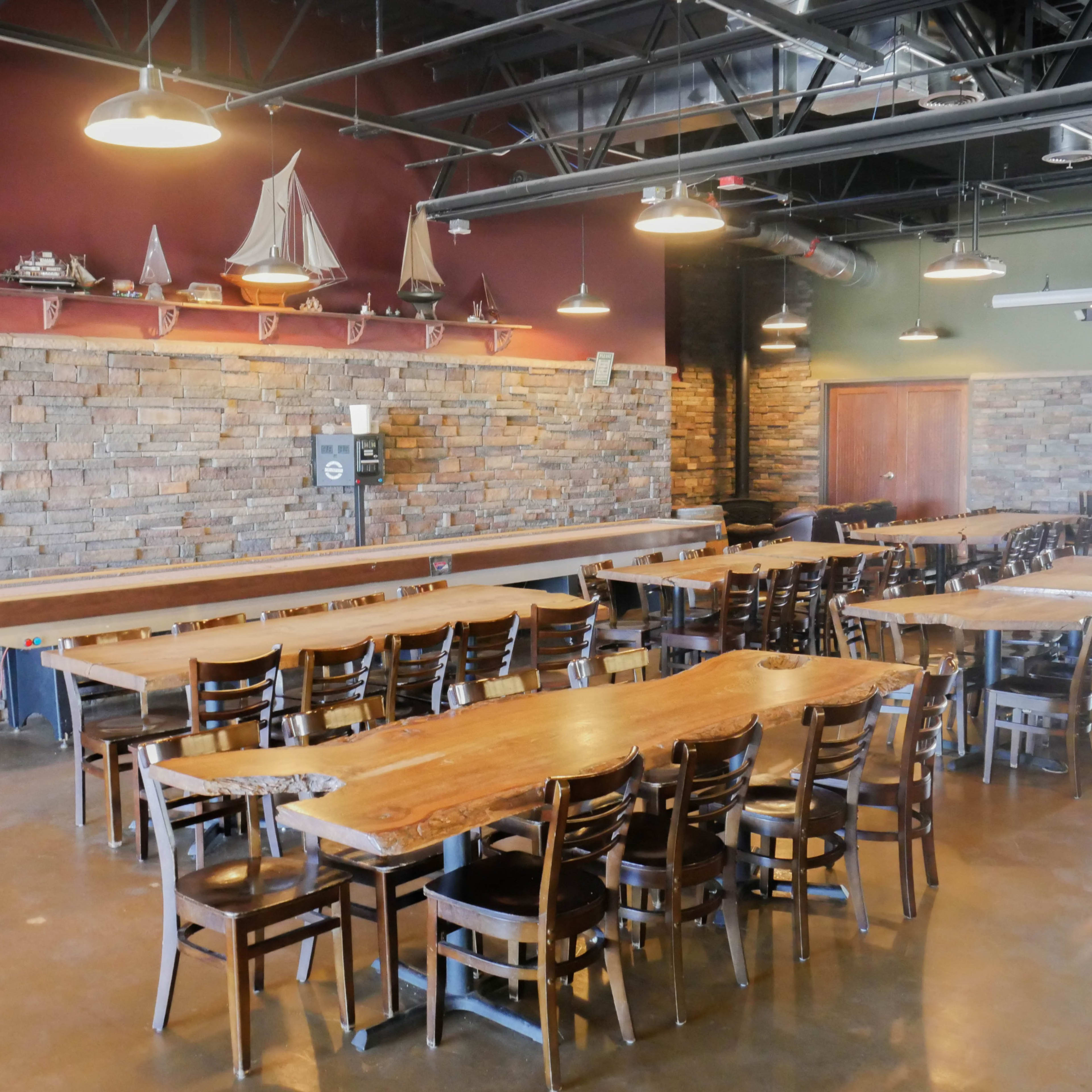A spacious restaurant interior featuring wooden tables and chairs arranged in a layout, with a stone accent wall and nautical decor on display.