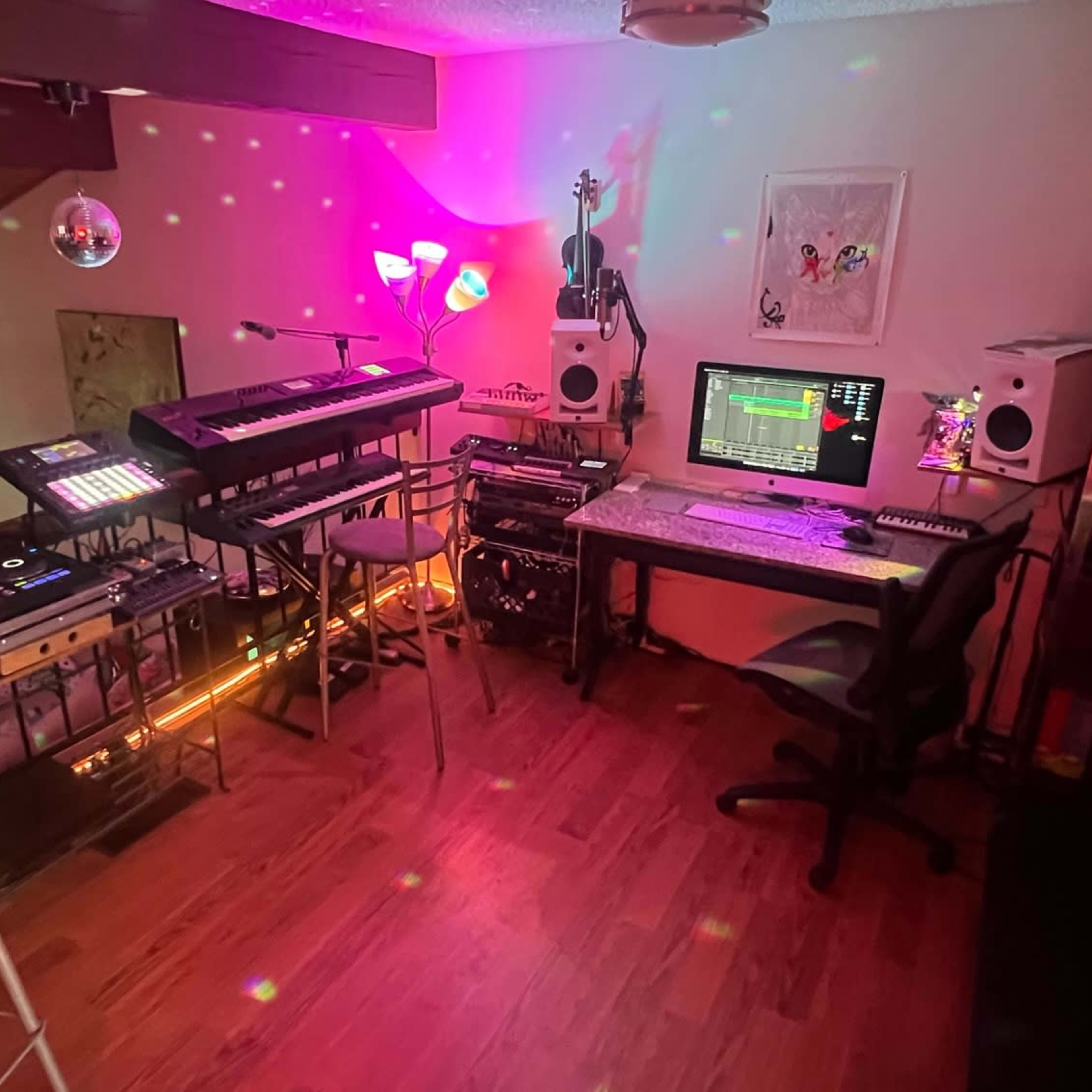 A home studio setup with keyboards, a computer, speakers, and DJ equipment surrounded by colorful lights.