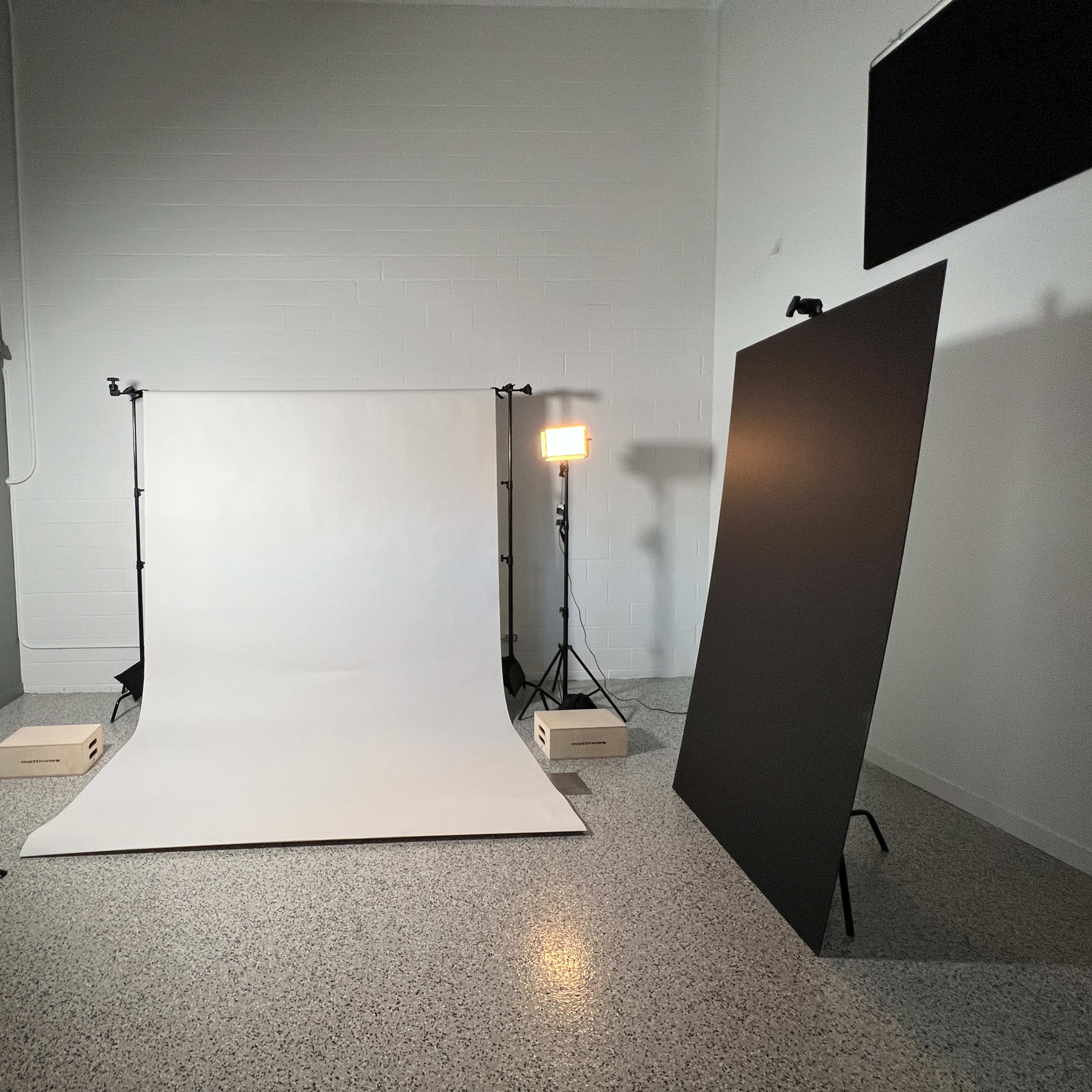 A photography studio setup with a white backdrop, softbox lights, and a black panel on the side.