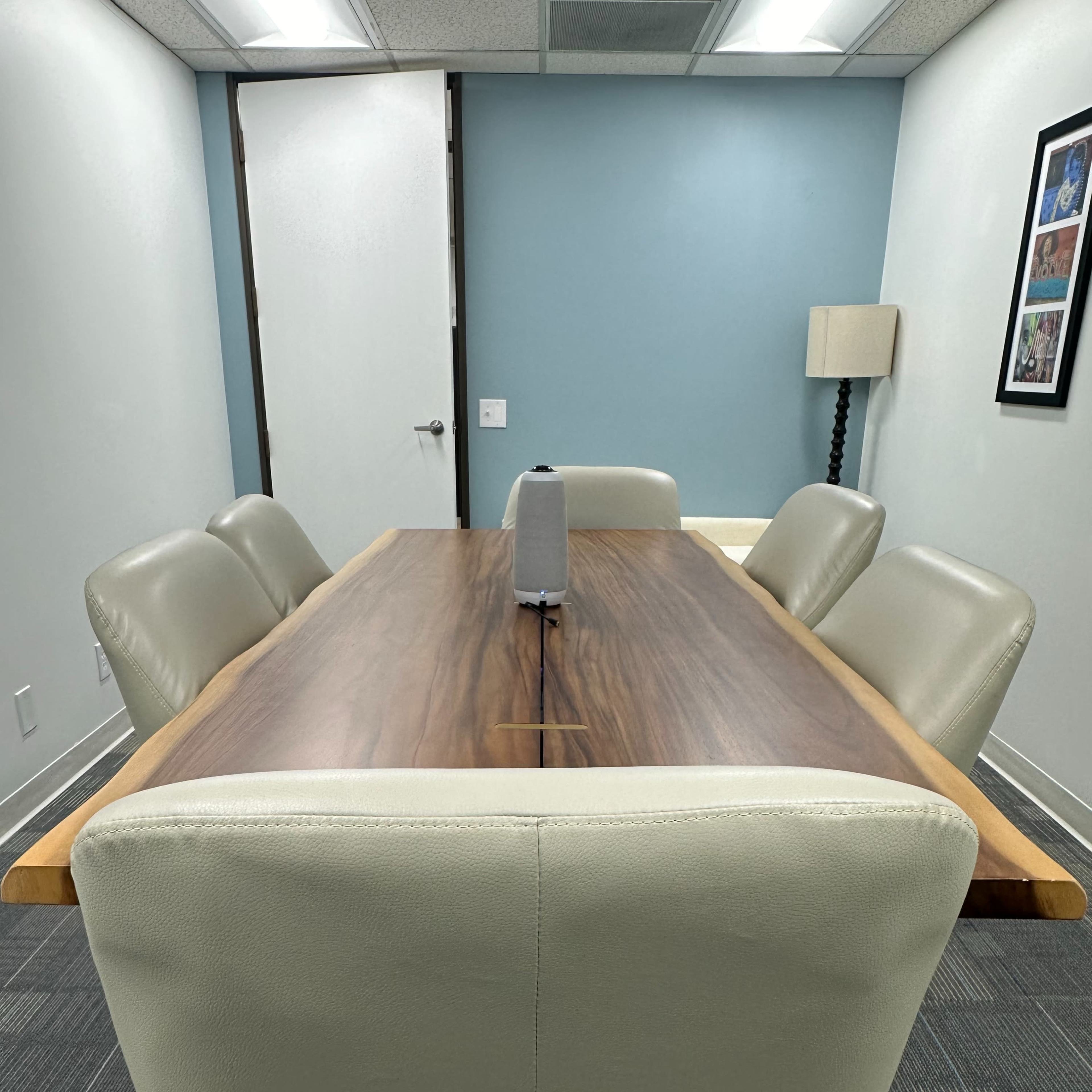 A conference room features a long wooden table with a central microphone and leather chairs arranged around it.