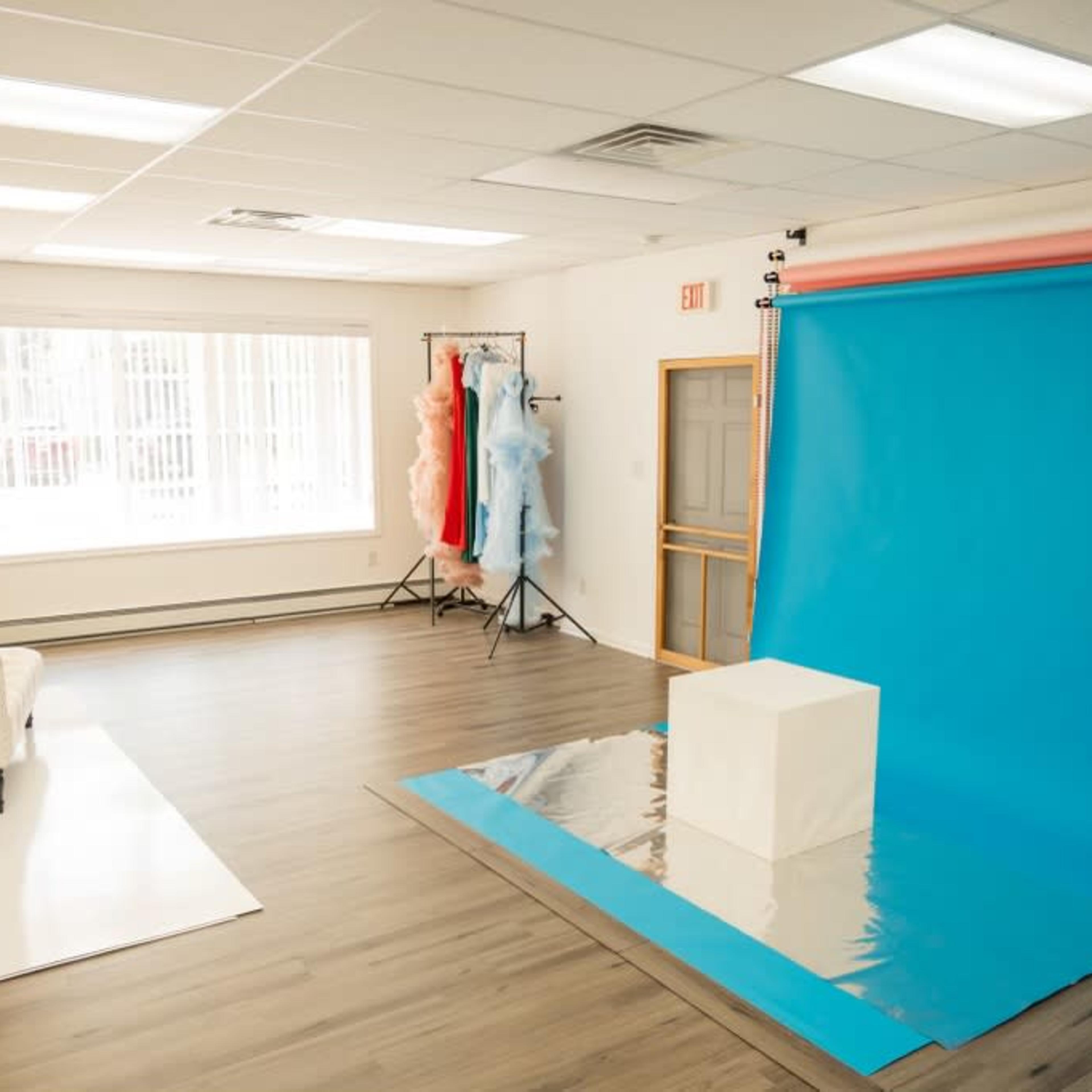 A photography studio with a blue backdrop, a white pedestal, and clothing racks with colorful garments.