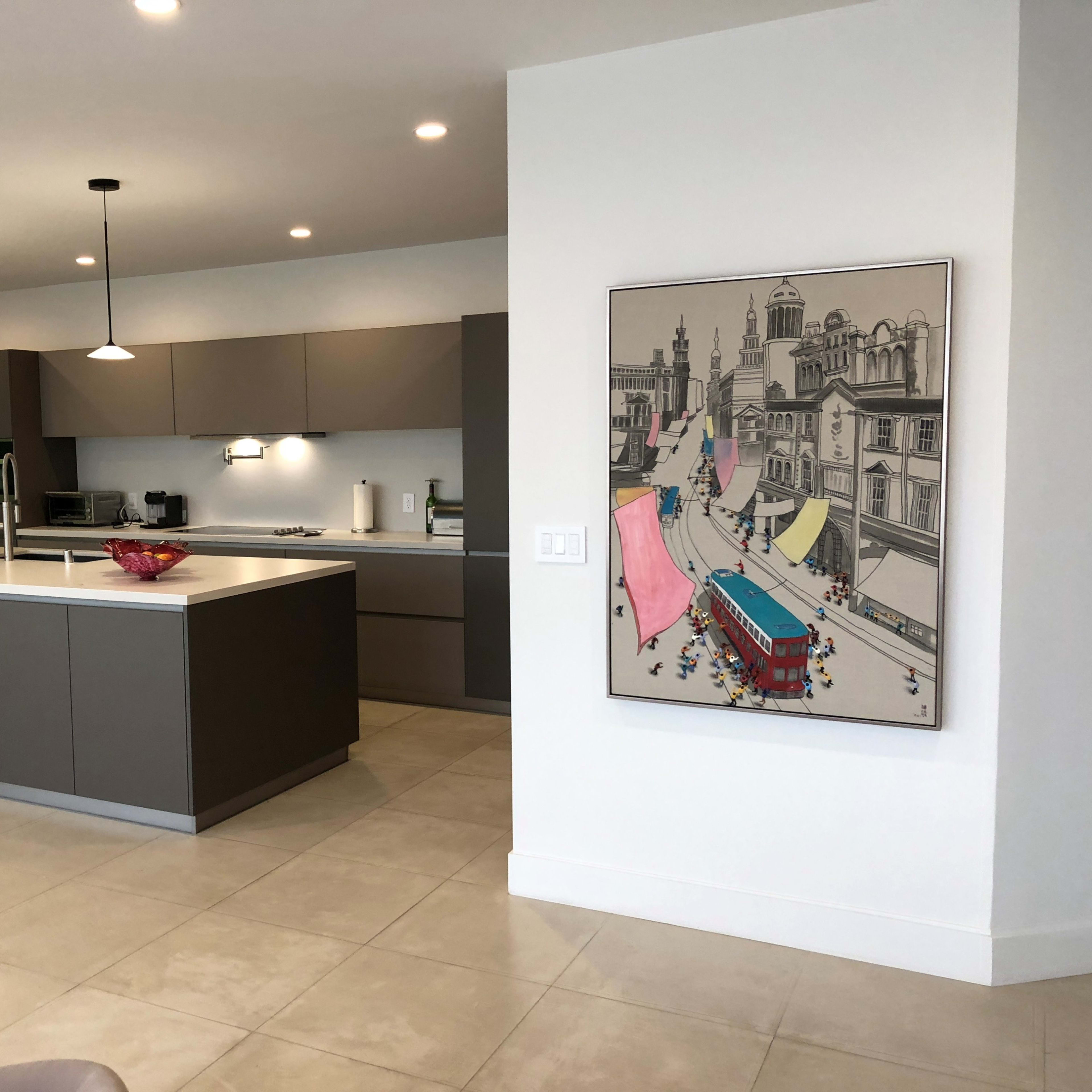 A modern kitchen with gray cabinetry and a large island, adjacent to a dining area featuring a colorful artwork on the wall.