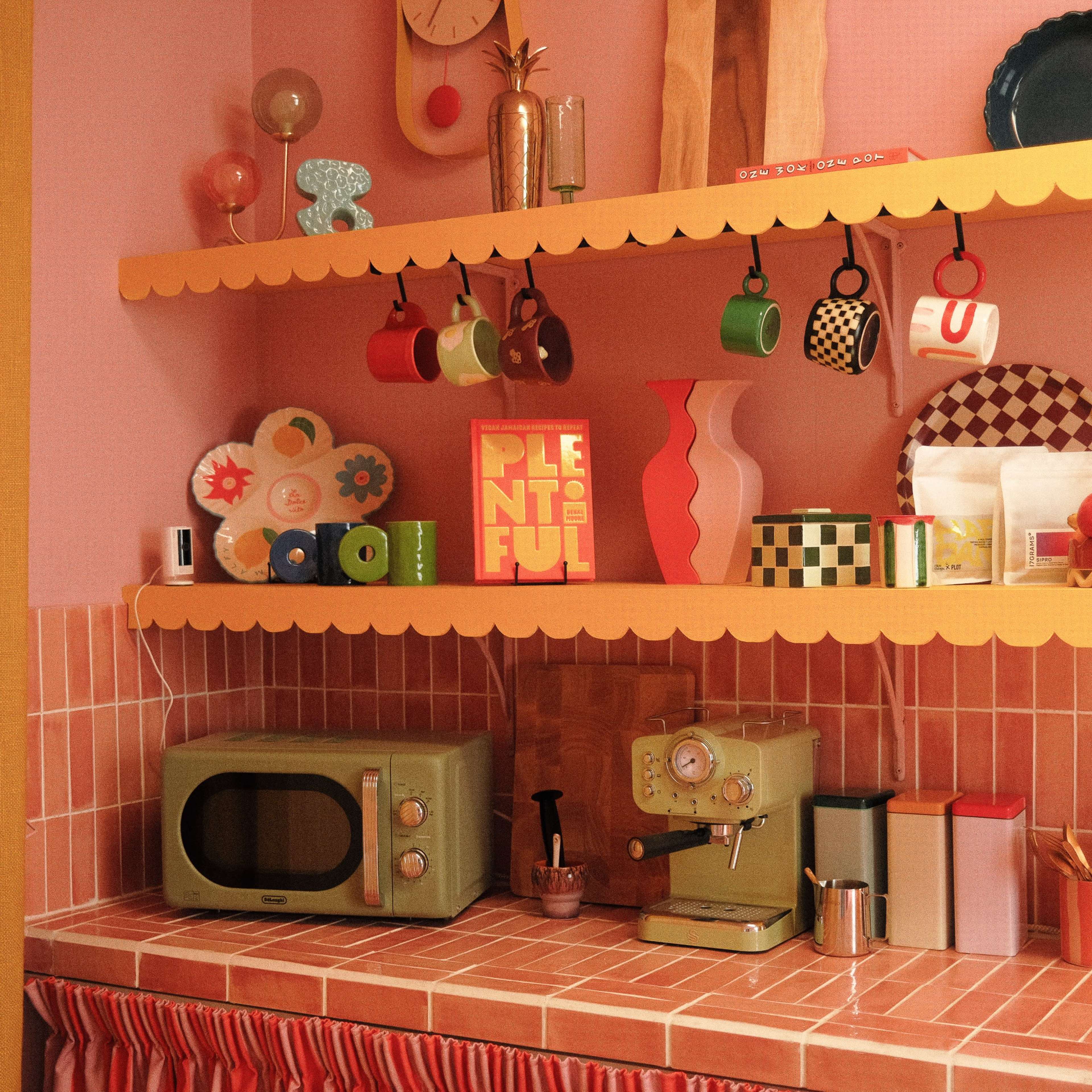 A vintage-style kitchen with pink walls, a checkered countertop, and colorful dishware arranged on shelves.