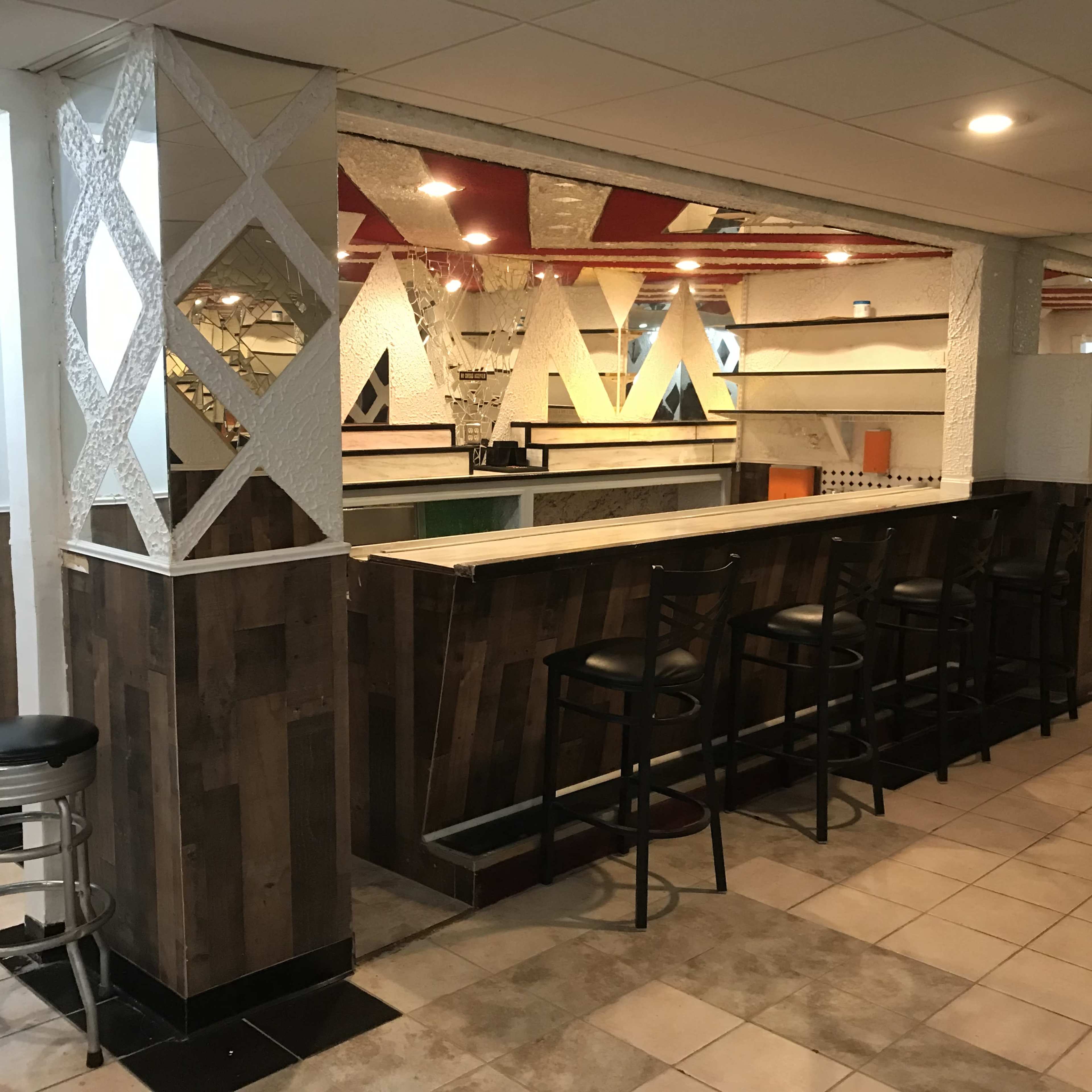 A bar area with a wooden counter and several black stools, featuring geometric partition designs and bright colored accents in the background.