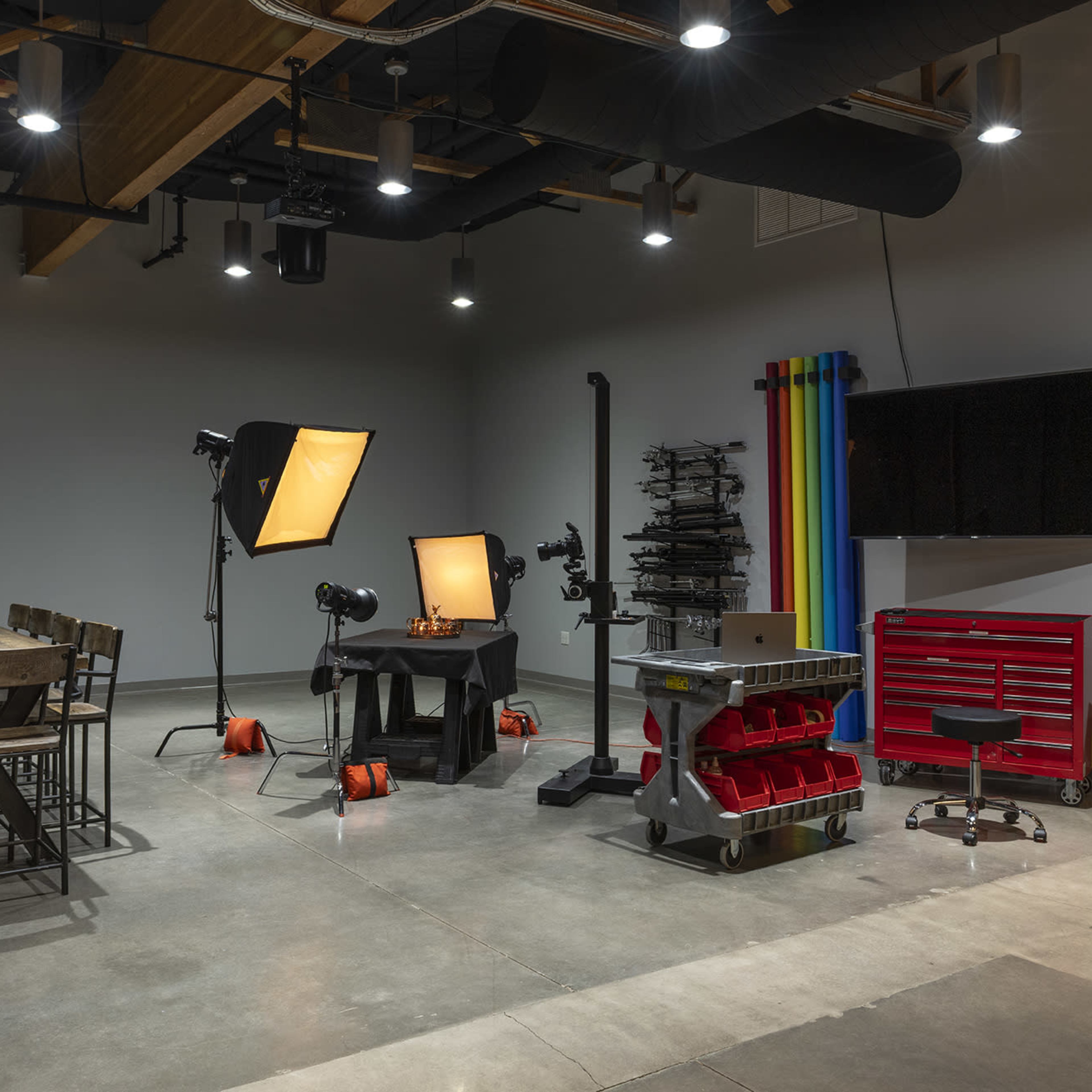 A photography studio equipped with lighting, a table, seating, and a workstation with tools.