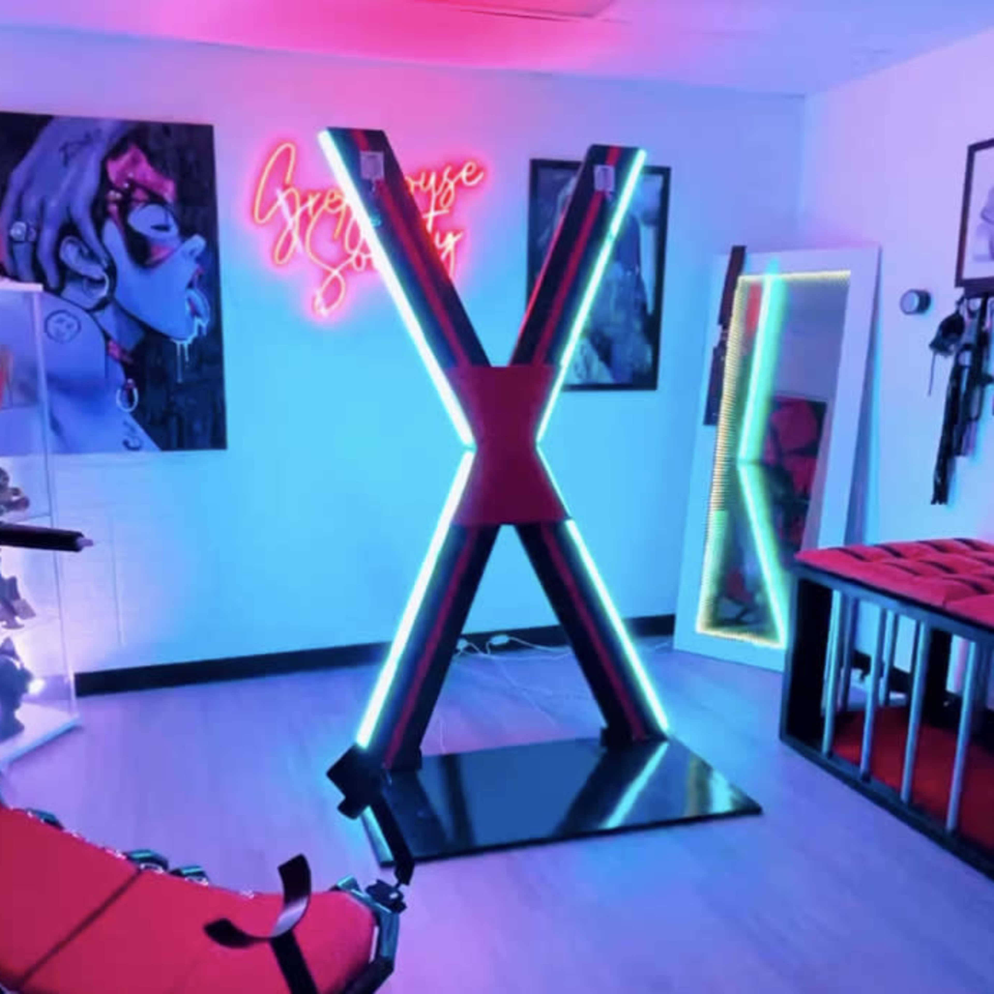 The room features vibrant neon lighting and modern furniture, including a red chair and a striking X-shaped display.